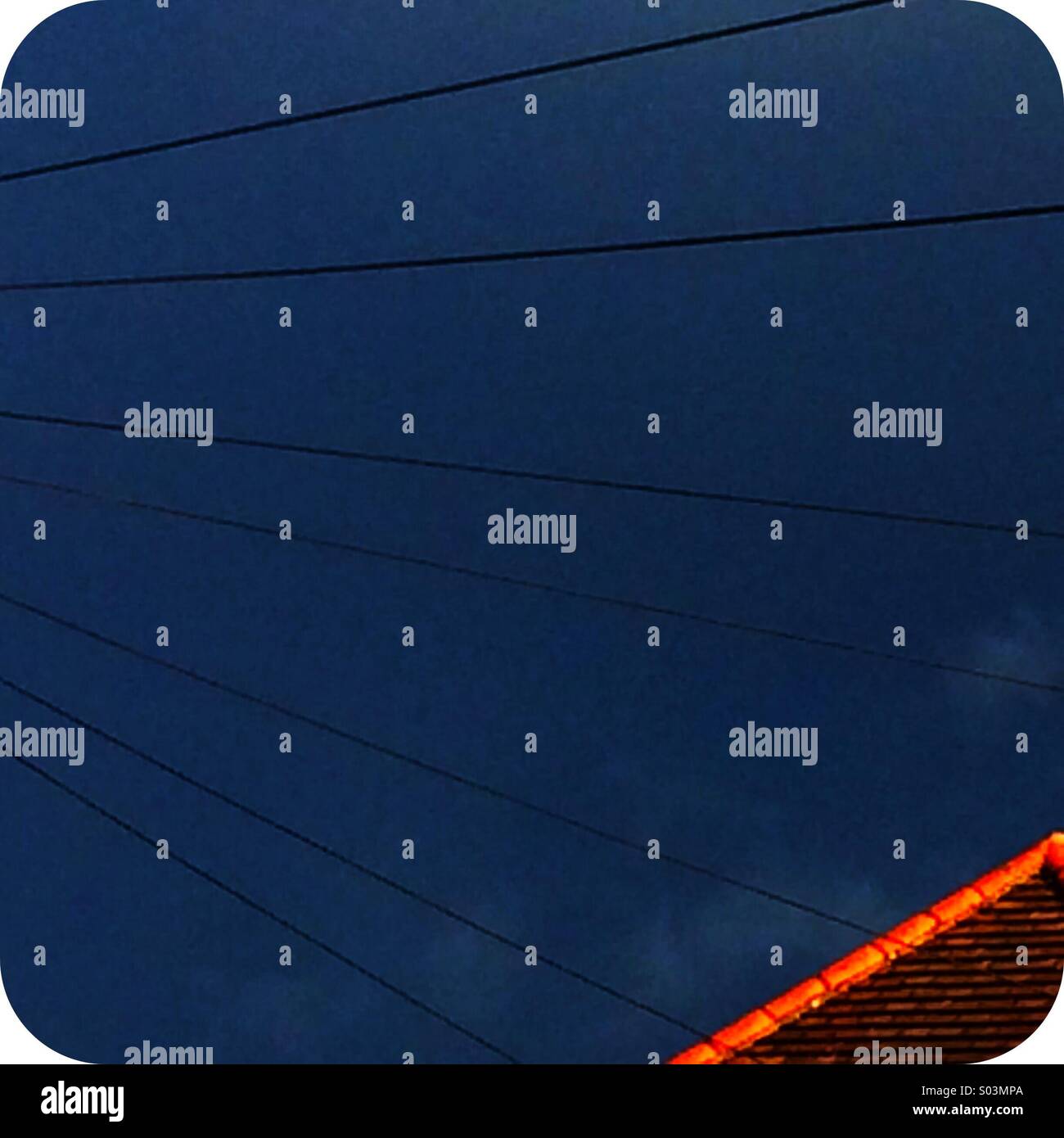 Telegraph lines across thundery sky with sunlight on house roof tiles - Smartphone Captured Stock Image