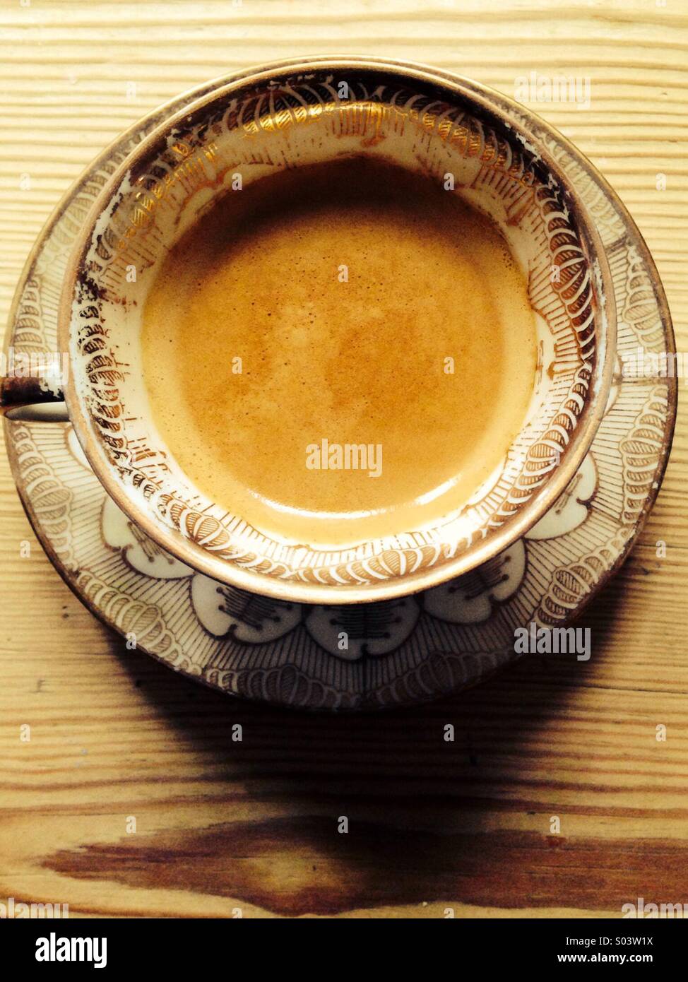 Coffee in French antique porcelain cup with gold and brown decoration on wooden table.. Stock Photo