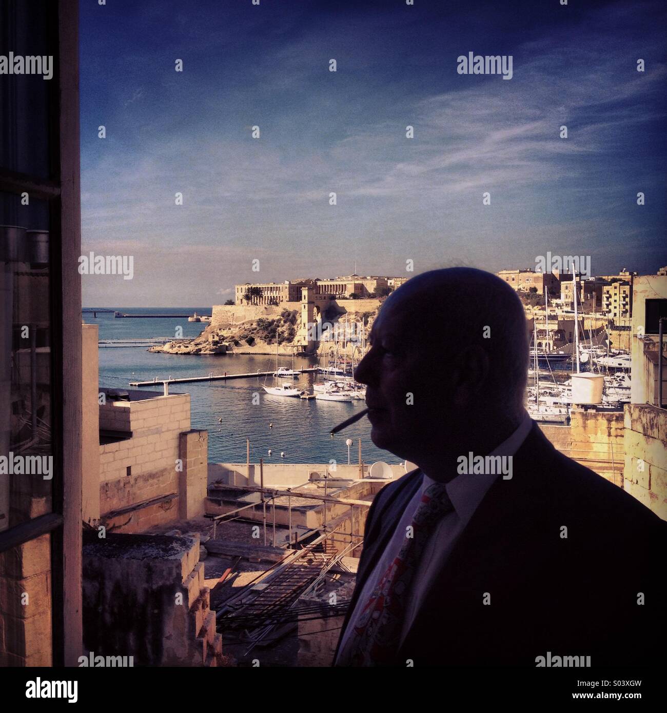 Man smoking at open window, overlooking Grand Harbour, Valletta, Malta Stock Photo