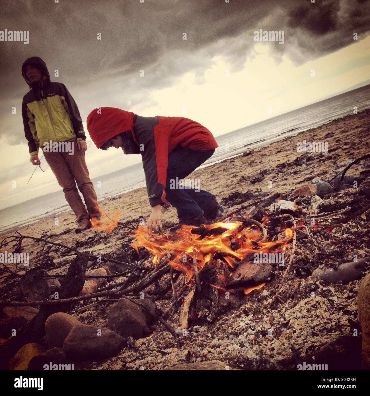 Mother and child on beach, with camp fire. Stock Photo