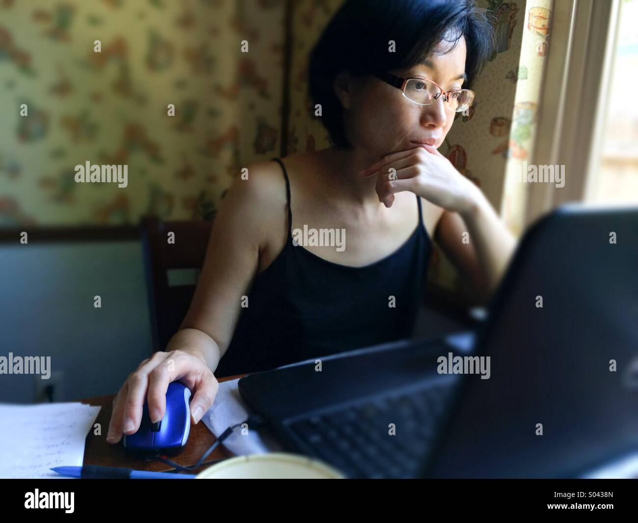 Asian woman working on a laptop computer at home - Smartphone Captured Stock Image