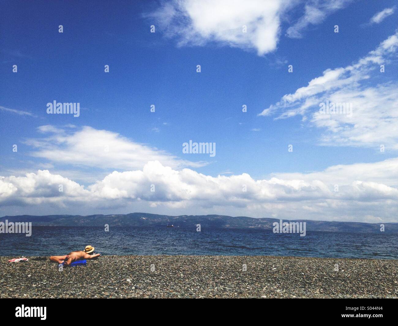 Brilliant sky with a lone bather on a rocky beach - Smartphone Captured Stock Image