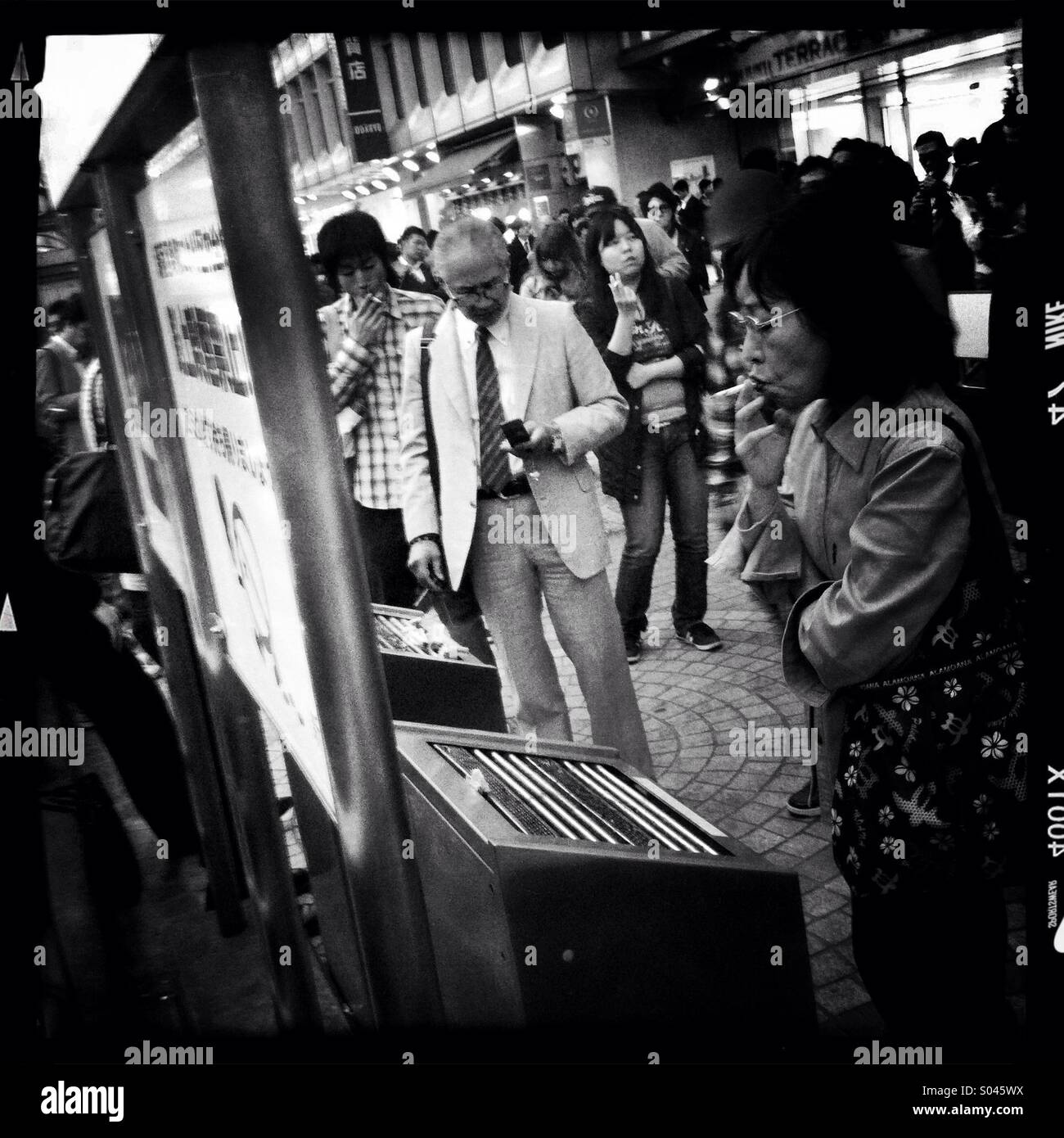 Smokers crowd into a designated smoking area in Shinjuku,Tokyo. Smoking while walking or on the street is banned in most wards in Tokyo. Stock Photo