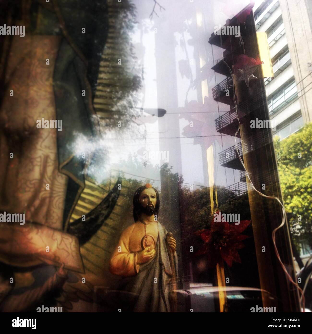 A building is reflected in an altar decorated with a sculpture of saint Jude Thaddeus in Parque España, Colonia Roma, Mexico City, Mexico Stock Photo