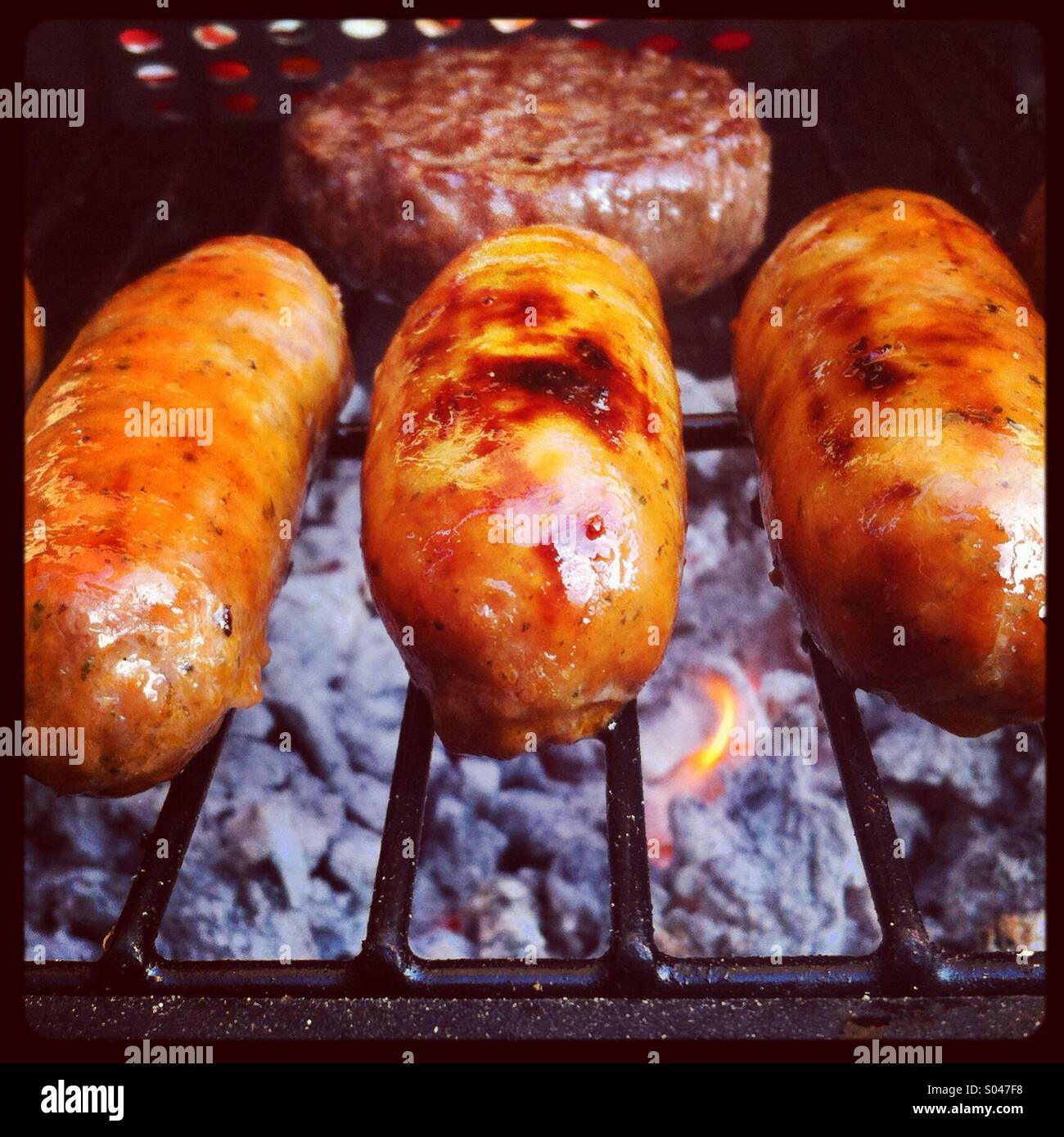 Three sausages and a burger cooking on a barbecue Stock Photo Alamy