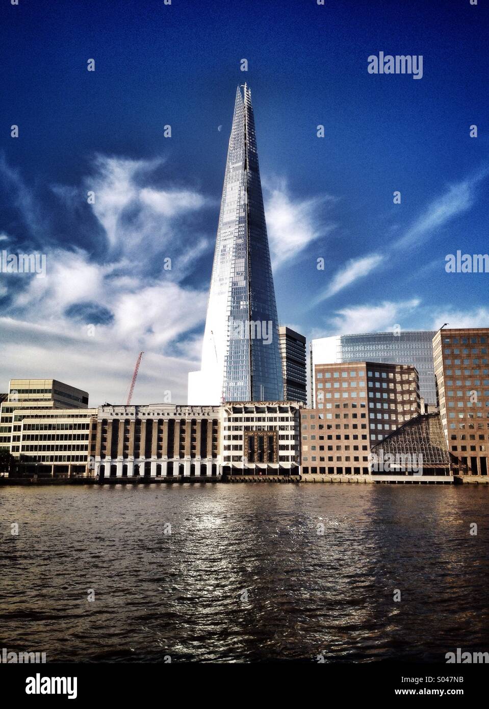 The Shard skyscraper in London with the river Thames in front of it and a blue sky and half moon behind it - Smartphone Captured Stock Image