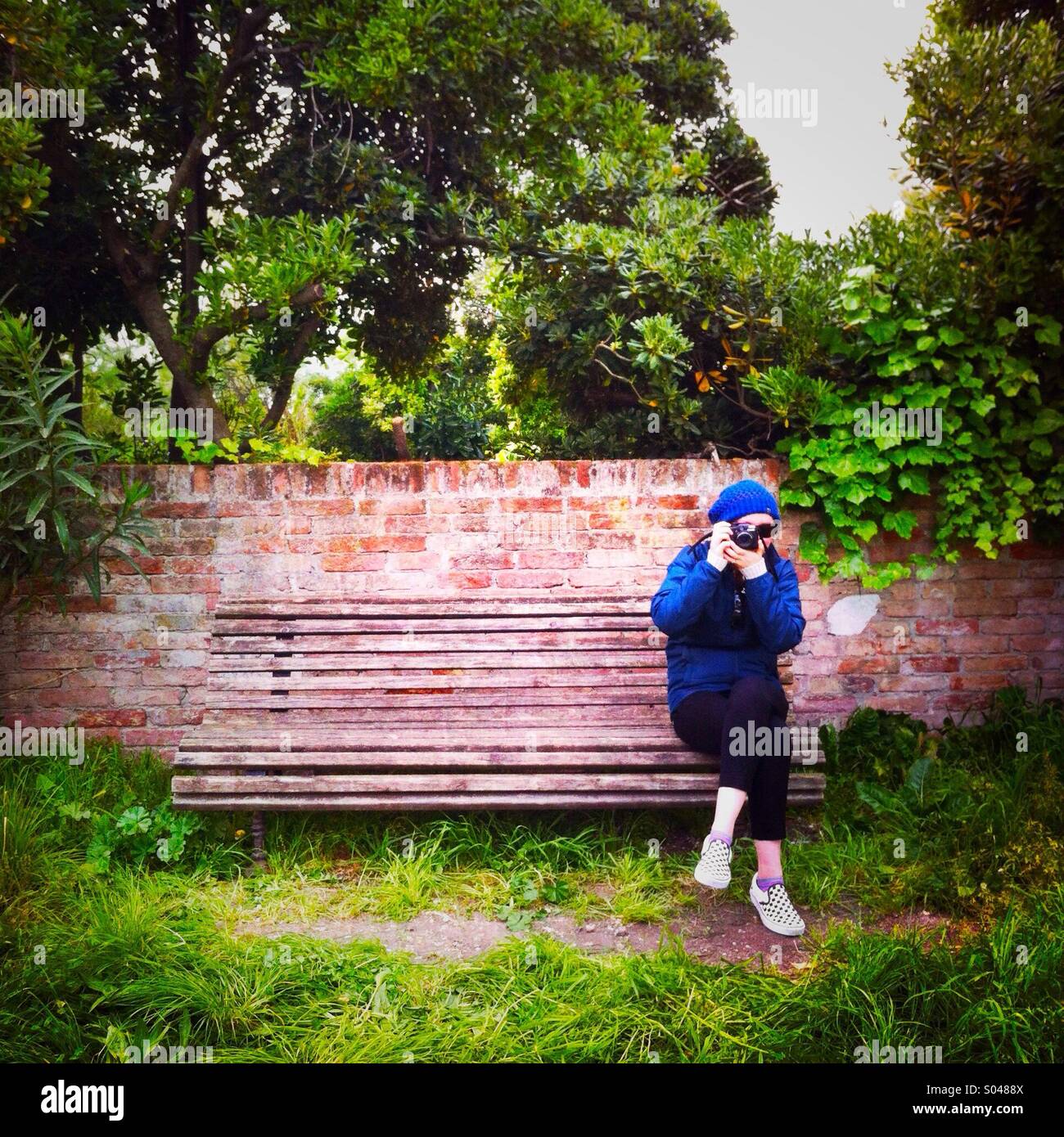 A young women sitting on a bench bench taking a photo. Venice Italy - Smartphone Captured Stock Image