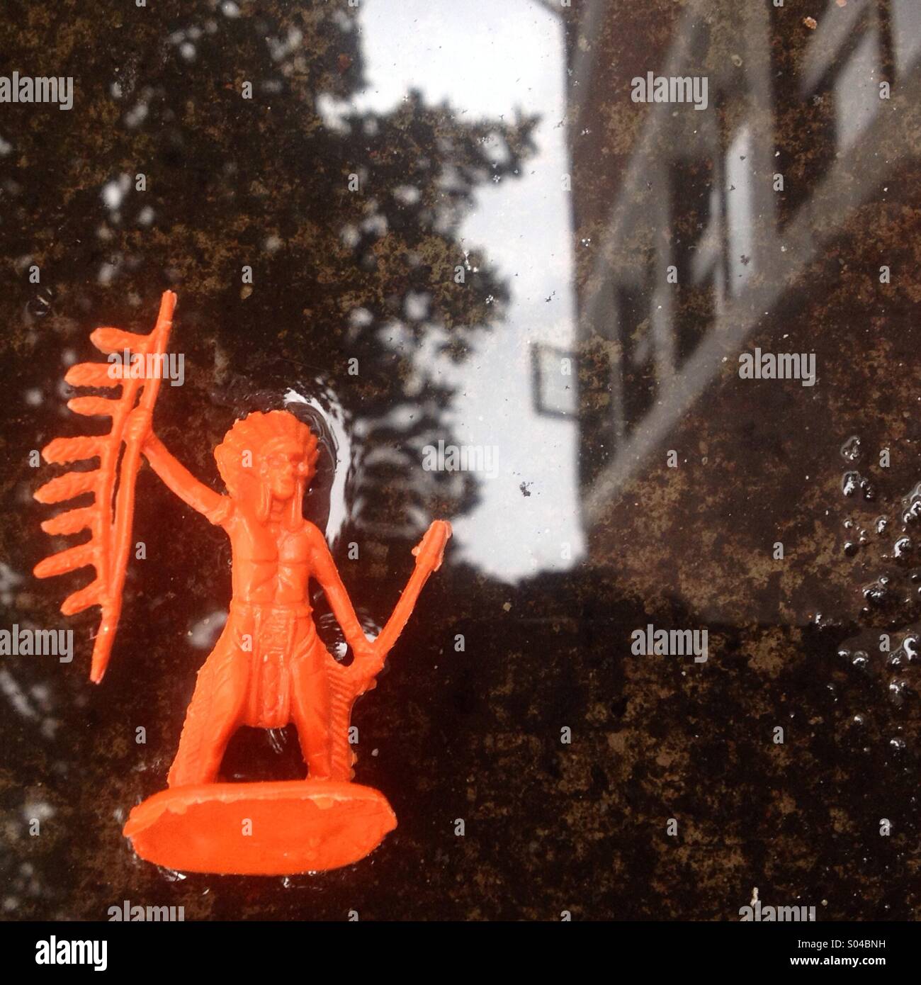 The reflection of a building in a puddle and an American Indian toy abandoned in a street of Colonia Roma, Mexico City, Mexico - Smartphone Captured Stock Image
