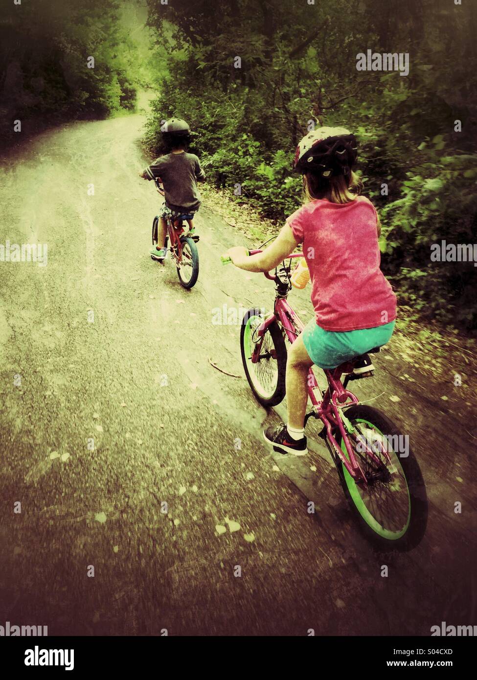 Two children ride their bicycles on a path through the woods. Stock Photo
