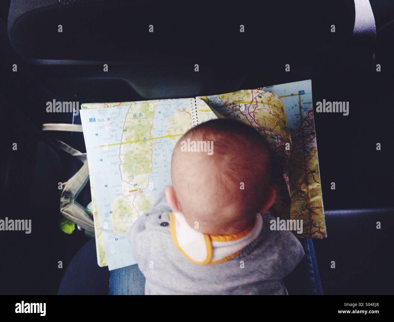 A baby planning a road trip with a map seen from above on the back seat in a car. Stock Photo