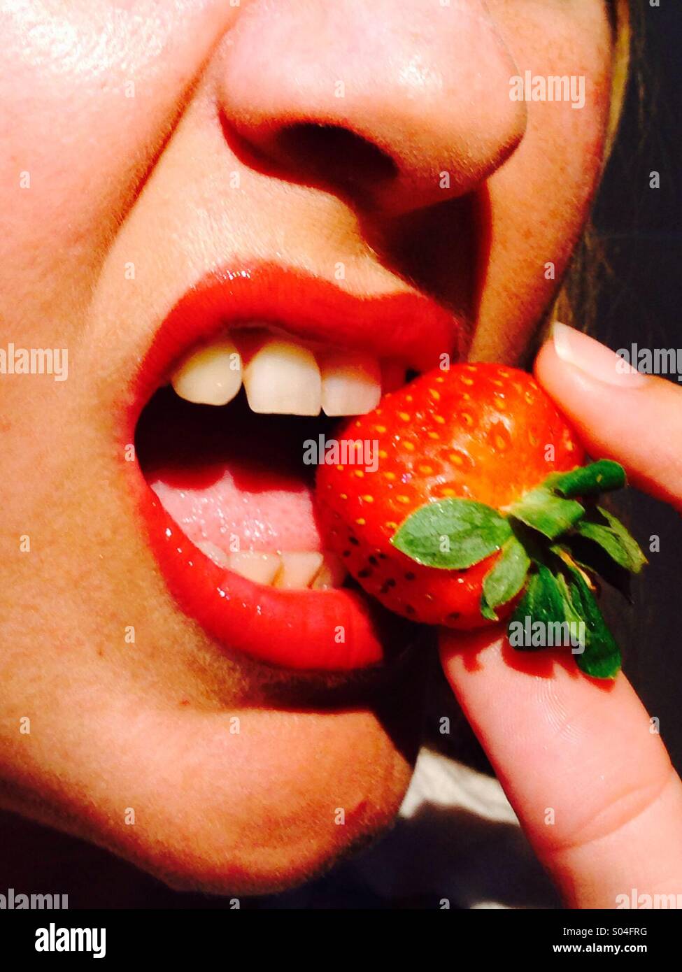 Strawberry being bitten between red lips Stock Photo
