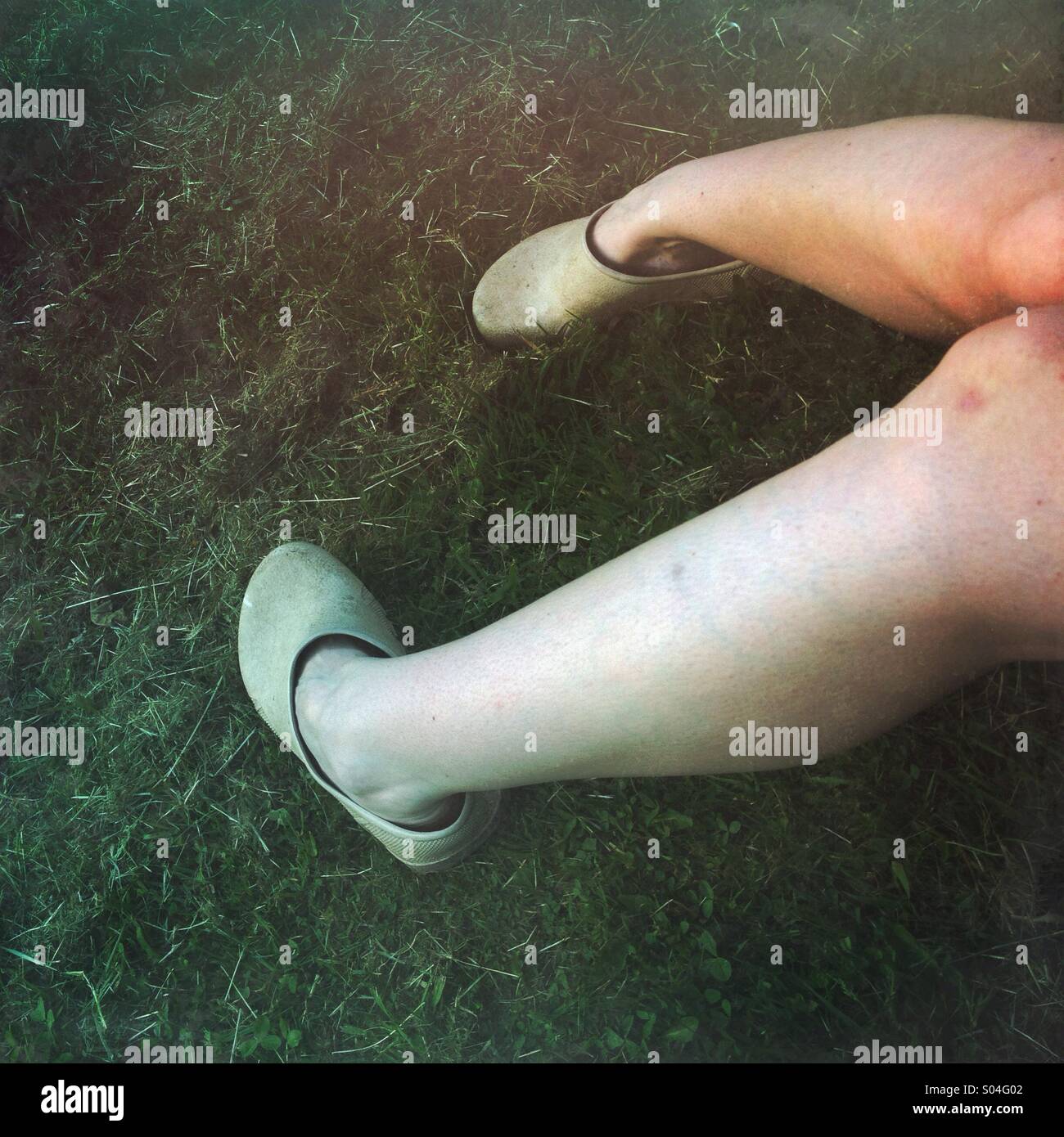 Woman's legs in grass wearing gardening clogs Stock Photo