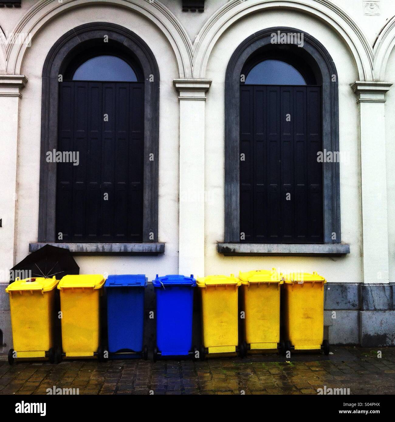 The trash bins of yellow and blue plastic lined up along the heritage white building in Brussels, Belgium, June 2014. - Smartphone Captured Stock Image