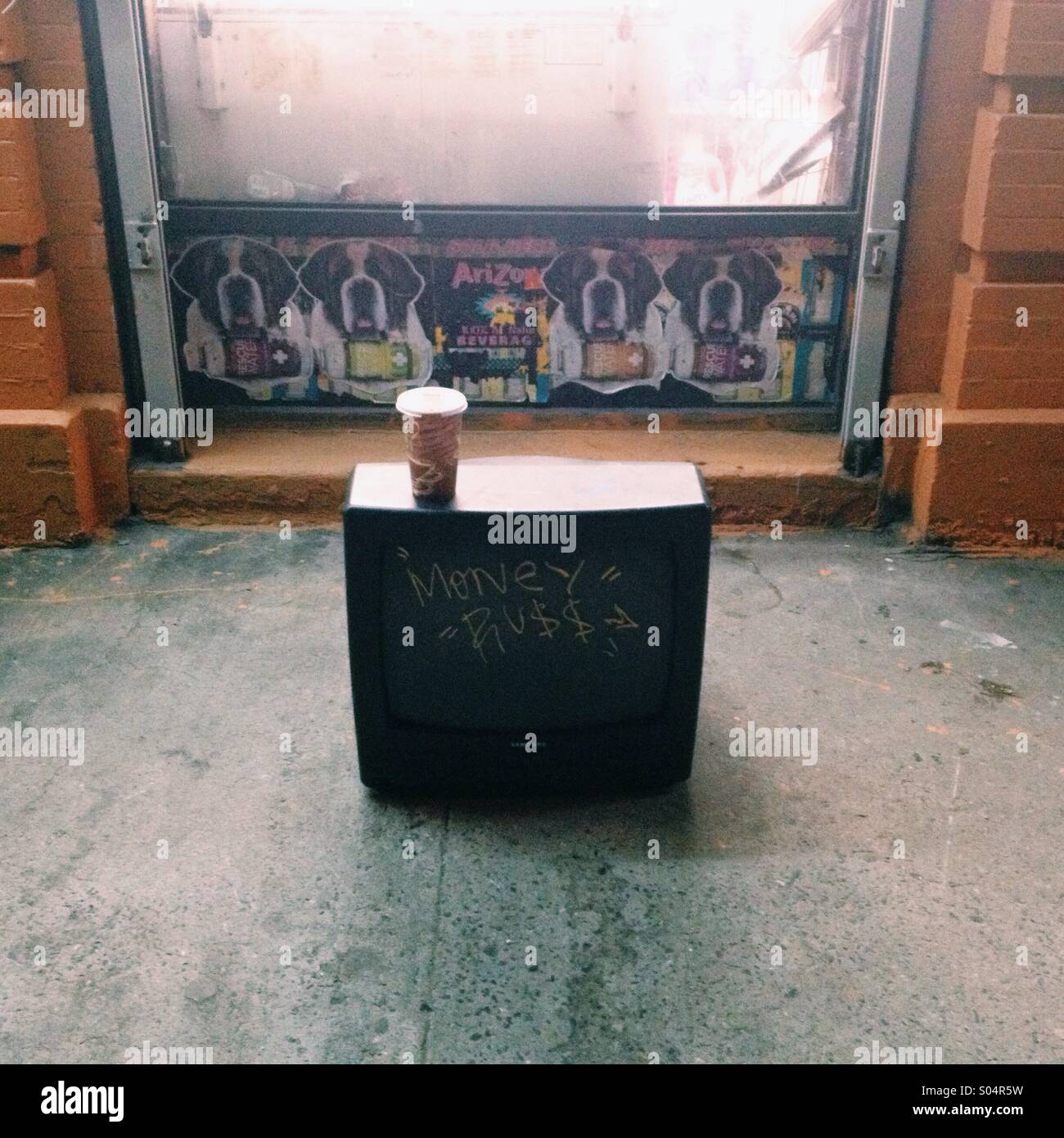 A graffitied television set with a cup of coffee on top of it sits outside a shop in the Brooklyn borough of New York City. Stock Photo