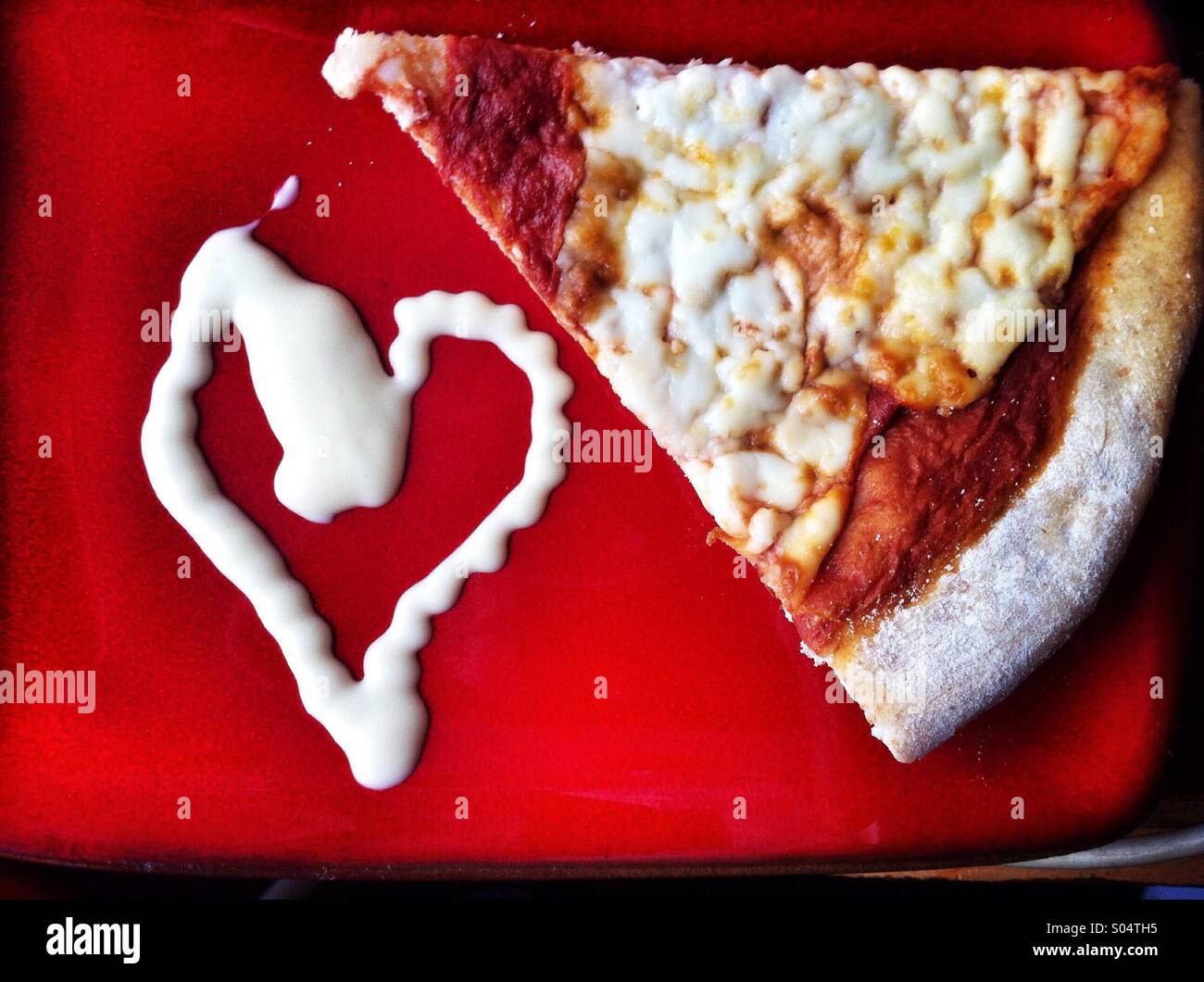 Pizza slice on a red plate with a salad cream heart - Smartphone Captured Stock Image
