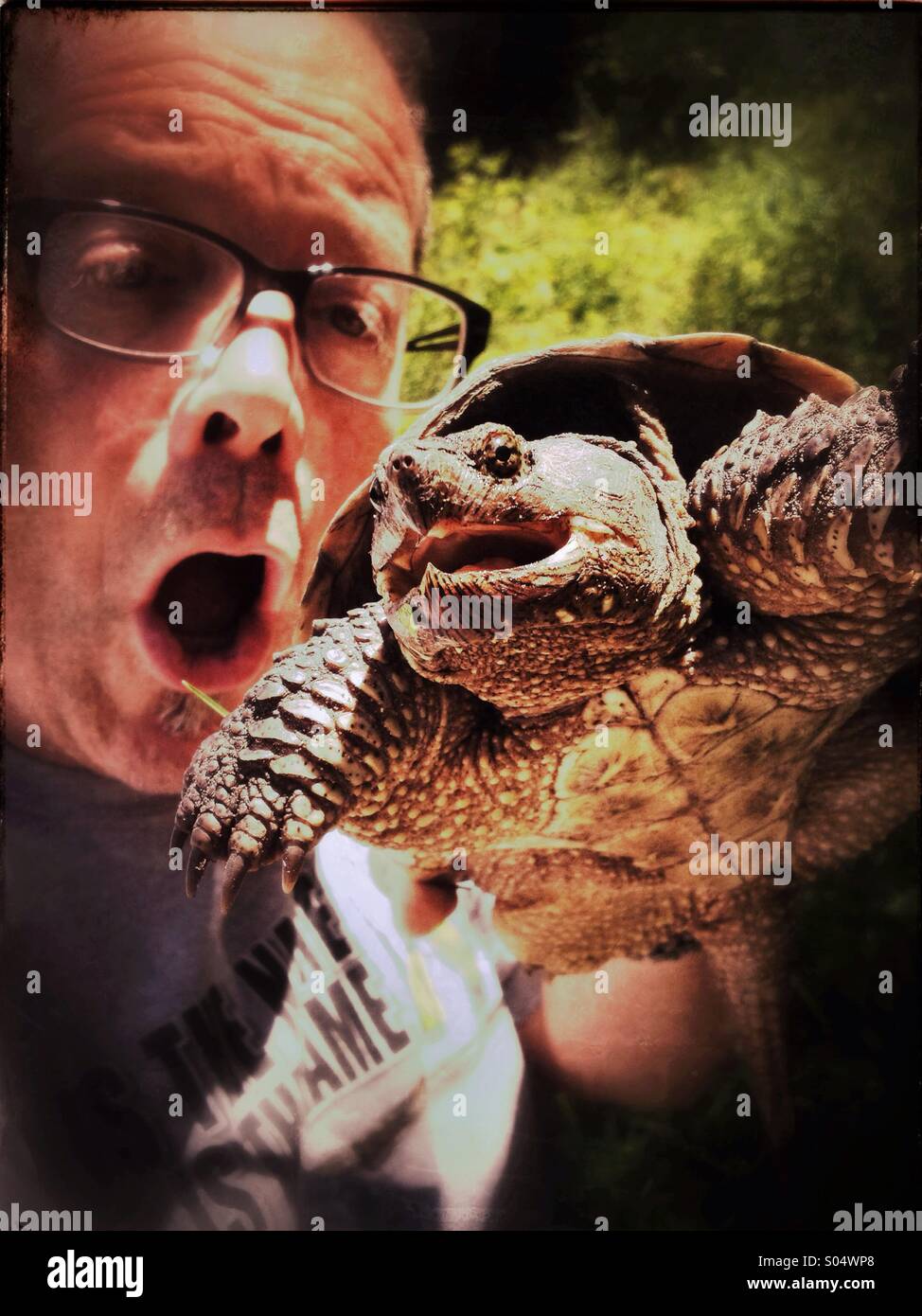 Man holding and looking at snapping turtle with open mouth - Smartphone Captured Stock Image