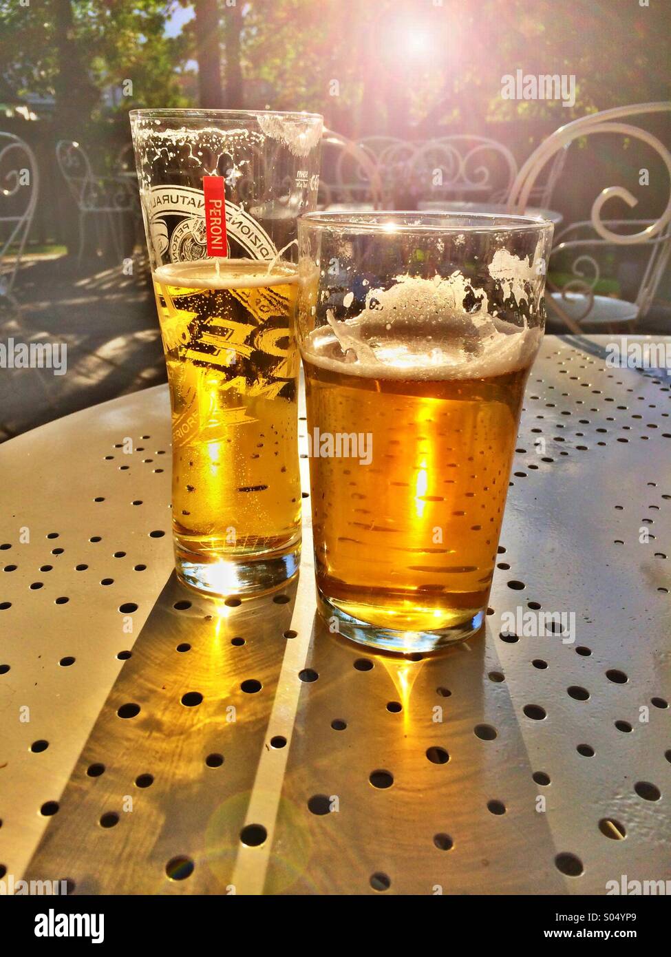 Partly drunk pint of lager and beer on a table backlit with lens flare - Smartphone Captured Stock Image