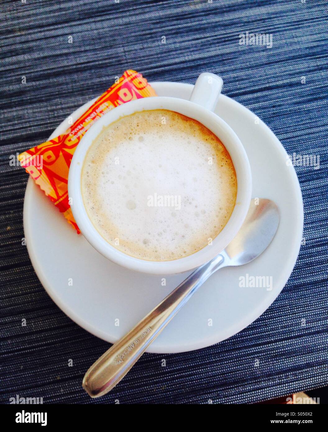 Coffee Cup and sugar packet.white coffee in white cup with spoon on white saucer and orange sugar packet. Stock Photo