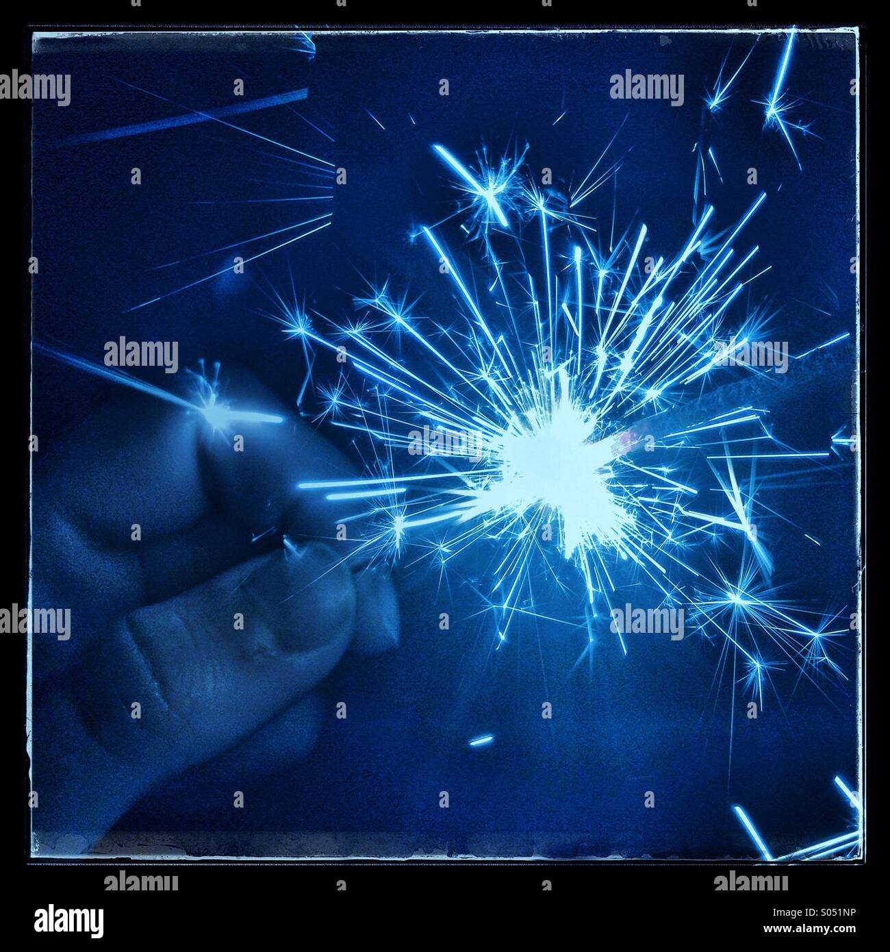 Hand holding lit sparkler fireworks with blue tint - Smartphone Captured Stock Image