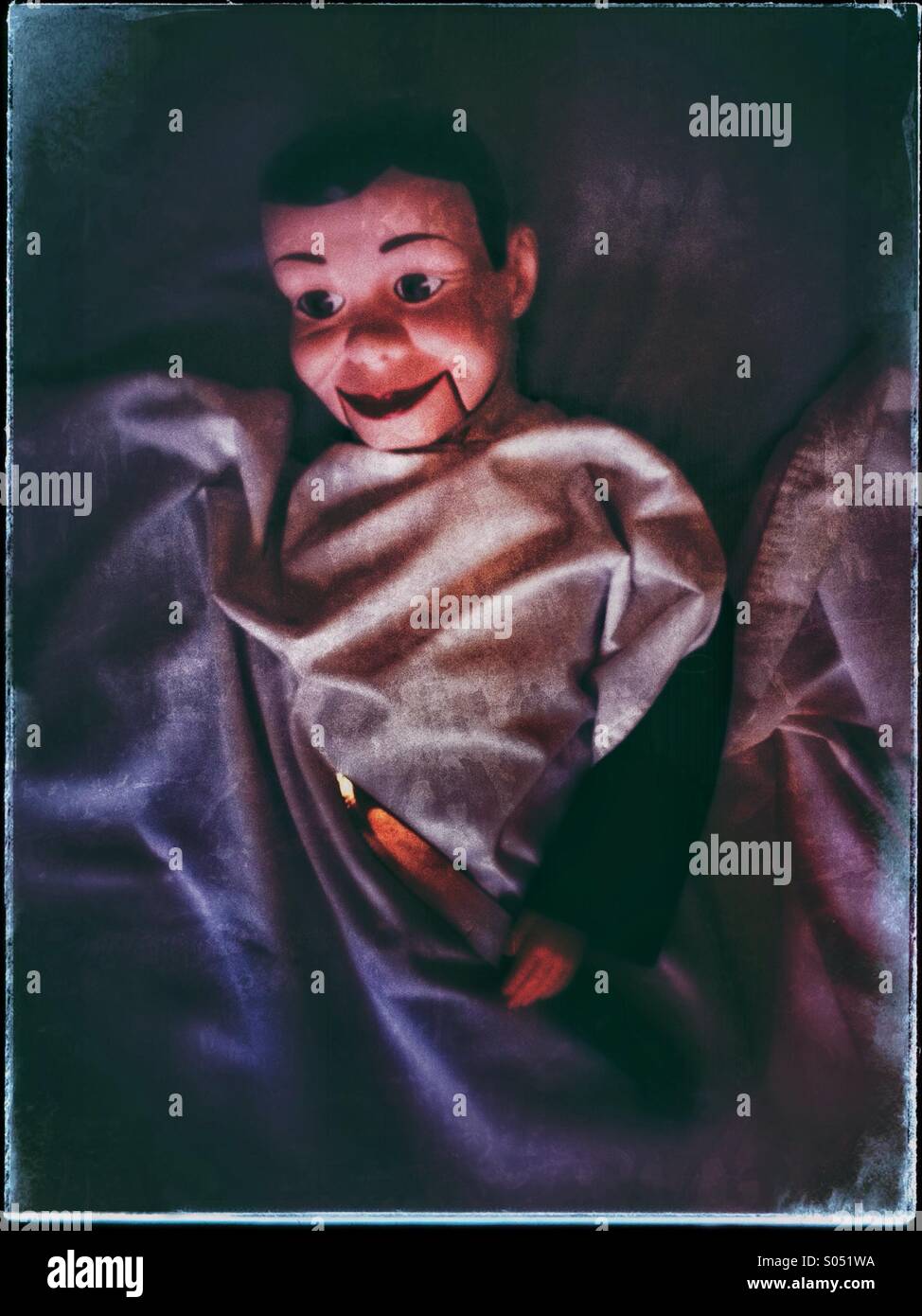 A Charlie McCarthy style ventriloquist doll in bed holding knife with scary lighting - Smartphone Captured Stock Image