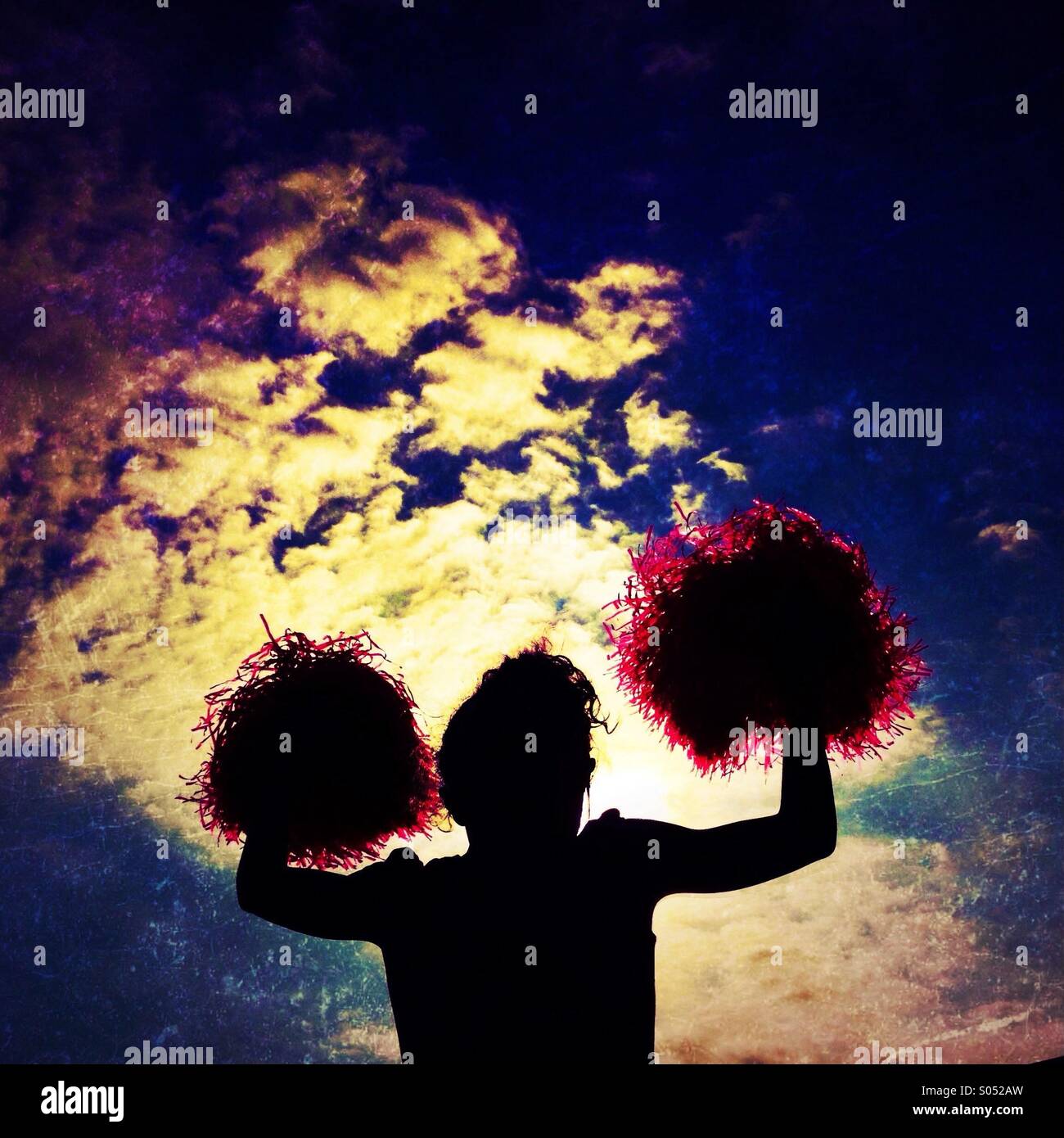Cheerleader waving Pom poms against dramatic sky Stock Photo