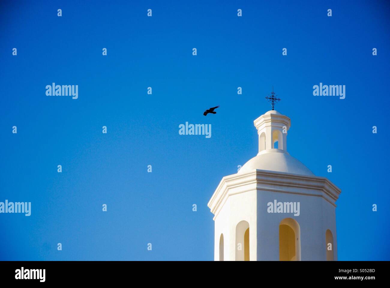 Bird flying by a bell tower of a church in the desert southwest USA. Stock Photo