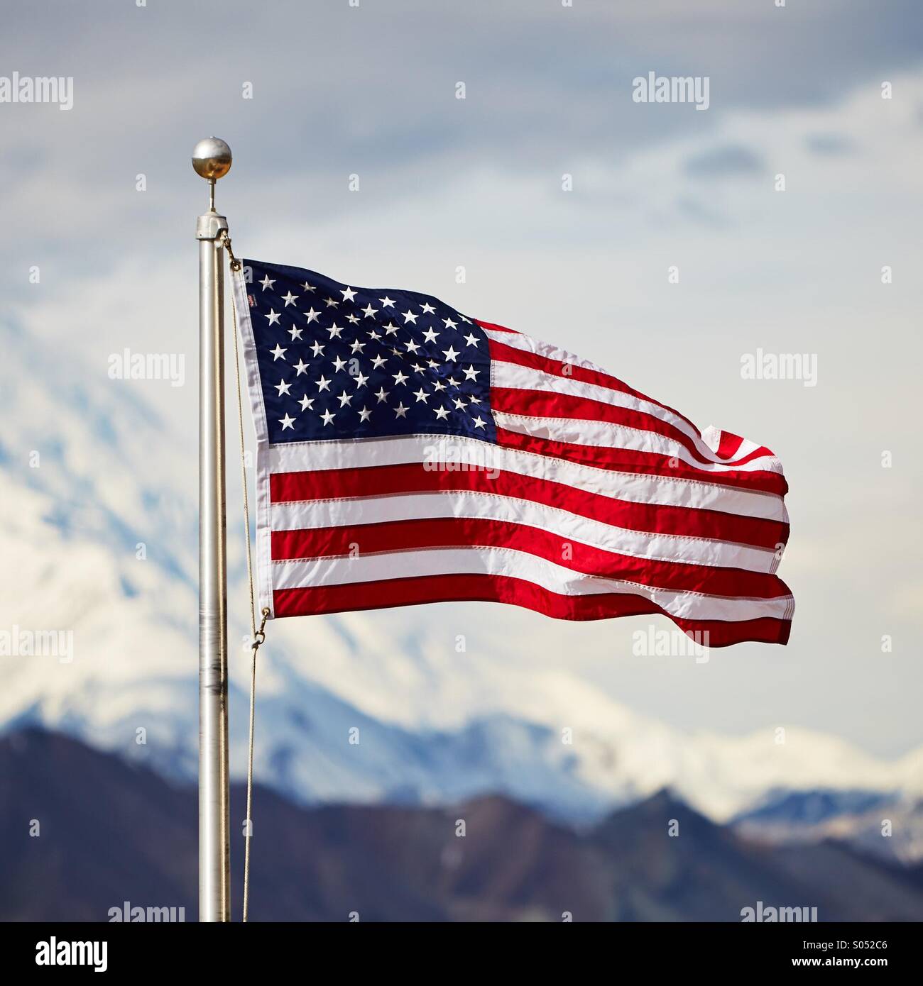 An American flag waves on a flag pole with snowy Alaskan Range mountains in the background. Stock Photo