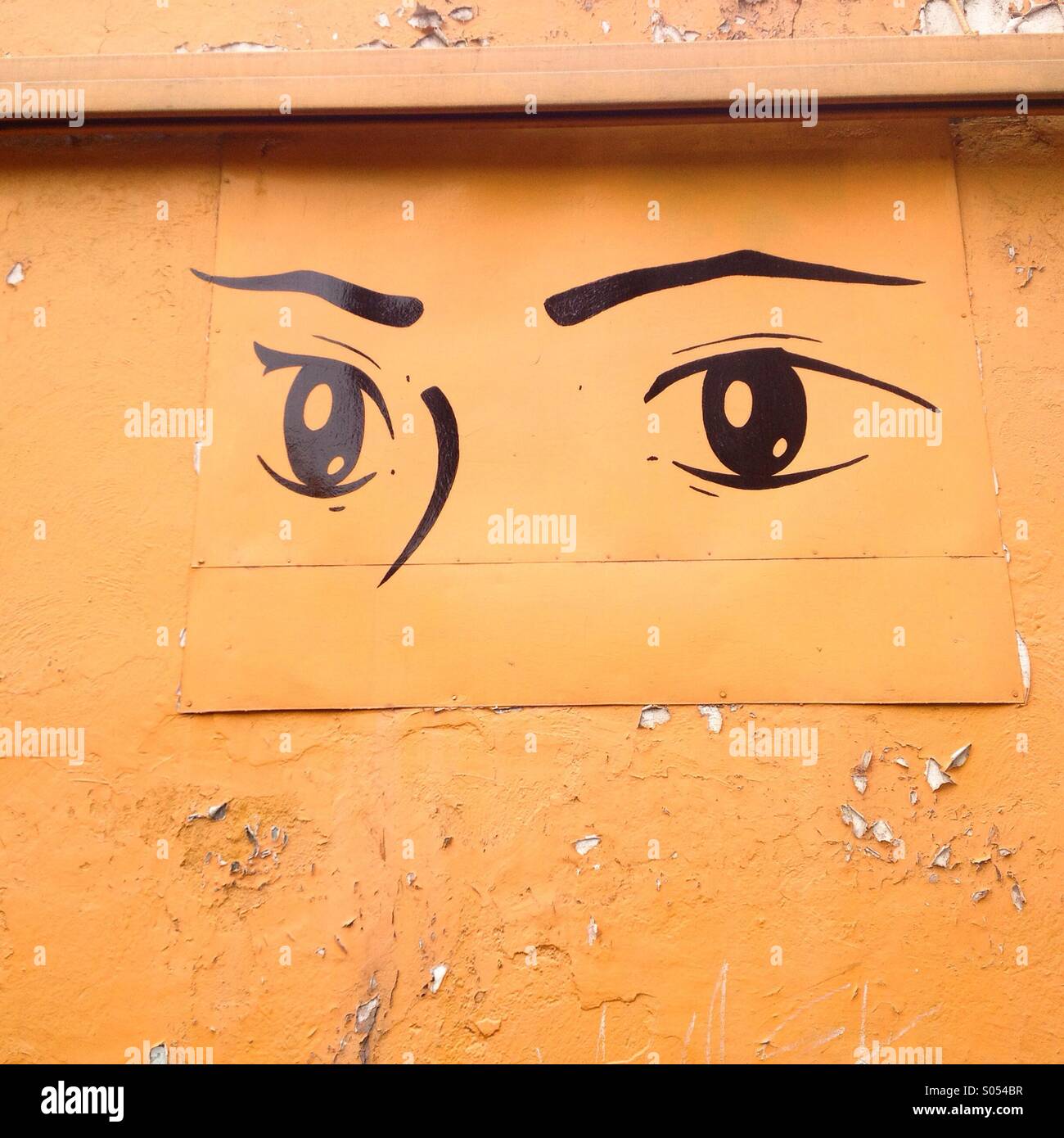 A painting of two eyes decorates an orange wall in Mexico City, Mexico Stock Photo