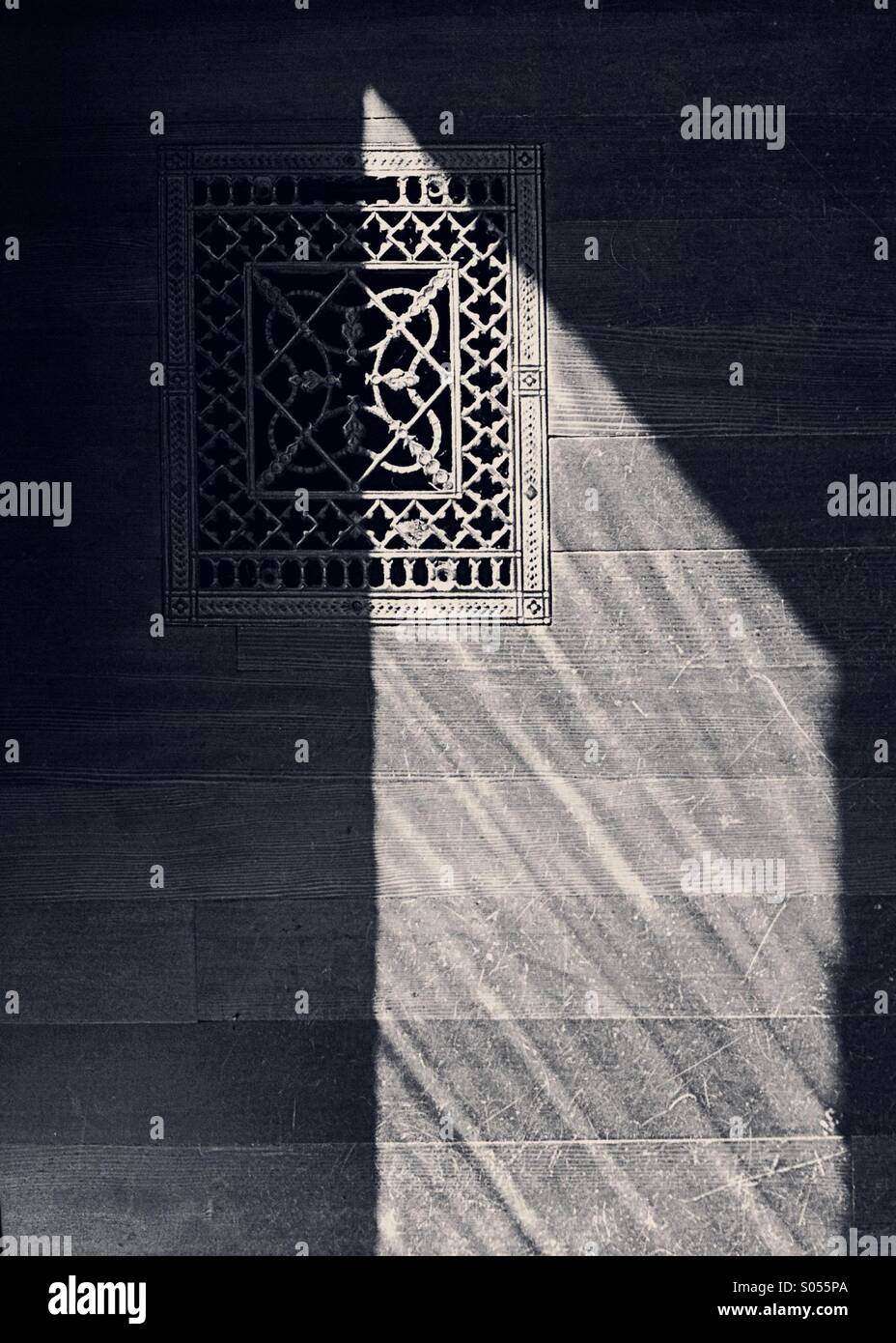 Pattern of light forms a triangular shape across an old wooden floor and antique metal heating vent. - Smartphone Captured Stock Image