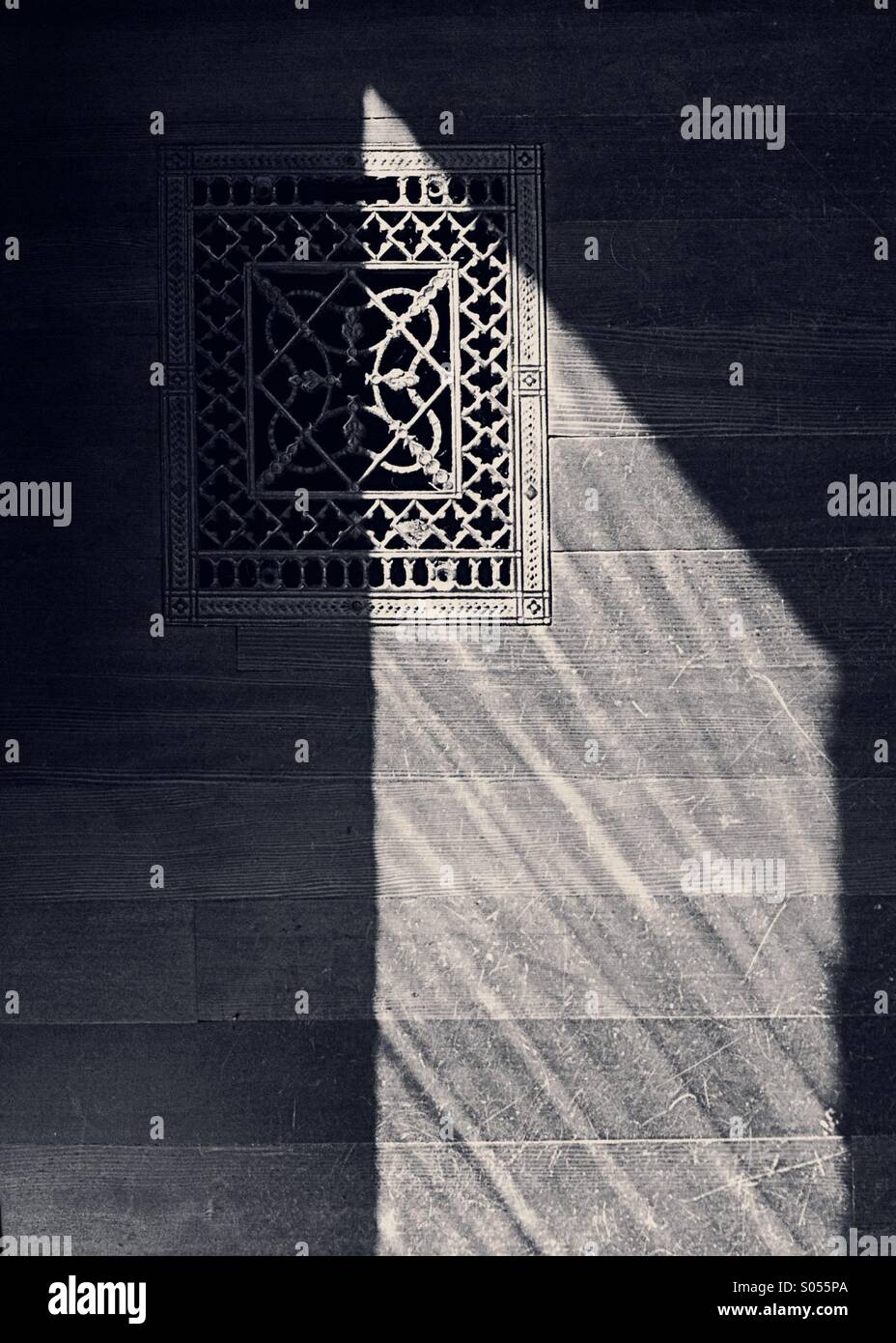 Pattern of light forms a triangular shape across an old wooden floor and antique metal heating vent. Stock Photo