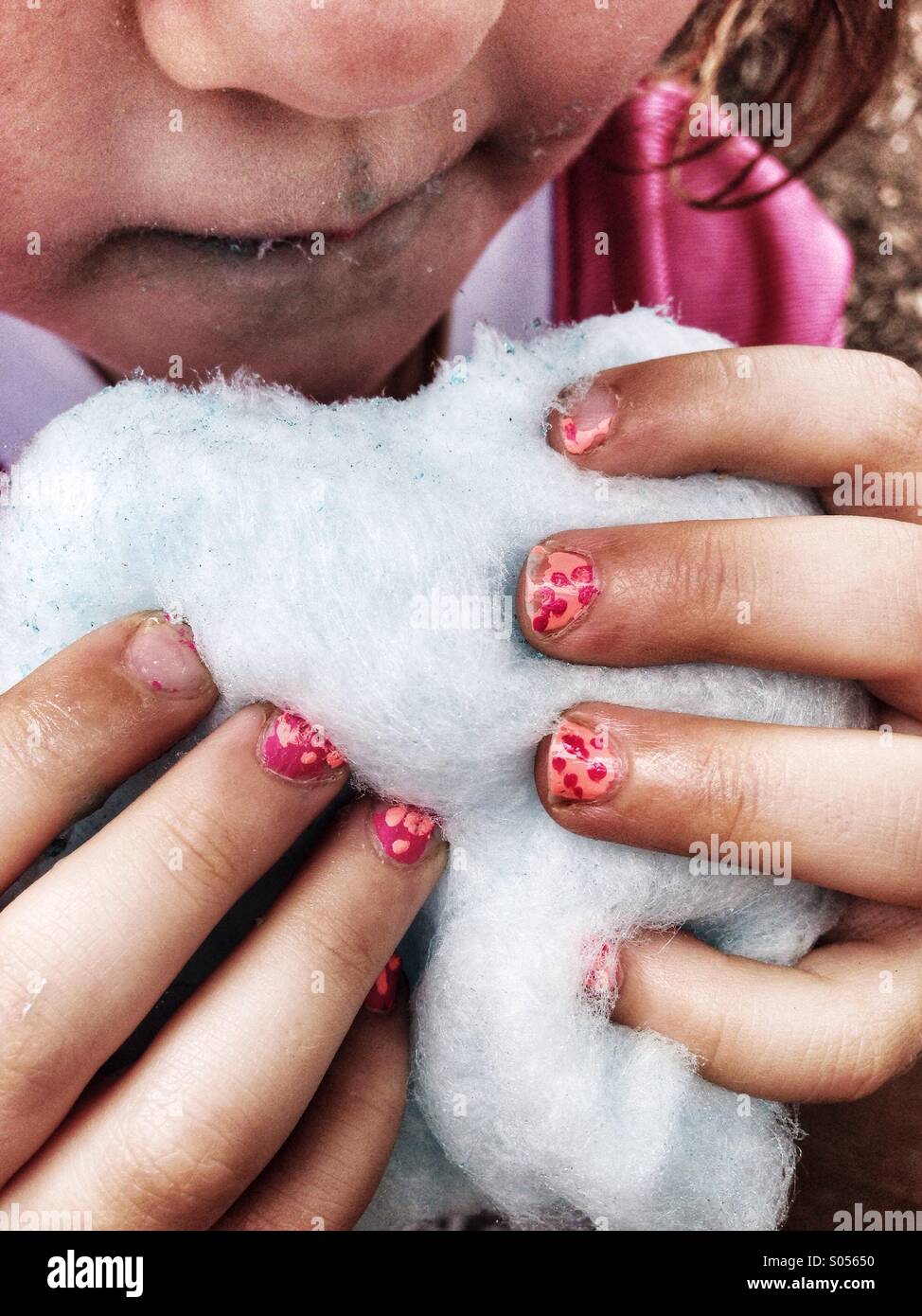 Little girl eats cotton candy with dirty hands and painted fingernails. Stock Photo