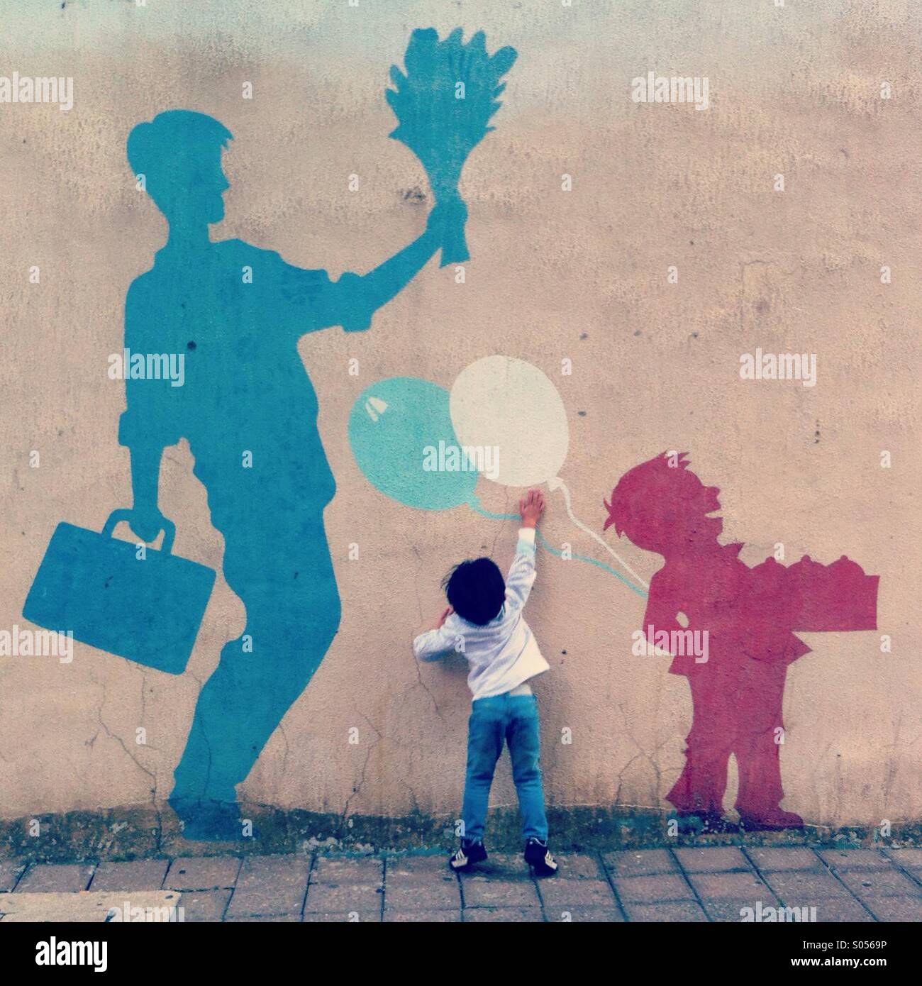 It's a photo of a child who is trying to catch a balloon painted on the wall. It's quite cute and funny - Smartphone Captured Stock Image