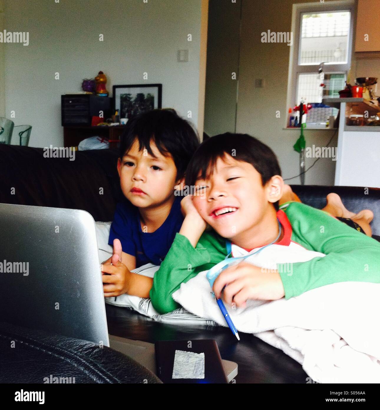It's a photo of 2 brothers who are watching a movie on a computer lap top. They ate on the sofa. One is smiling while the other one not - Smartphone Captured Stock Image
