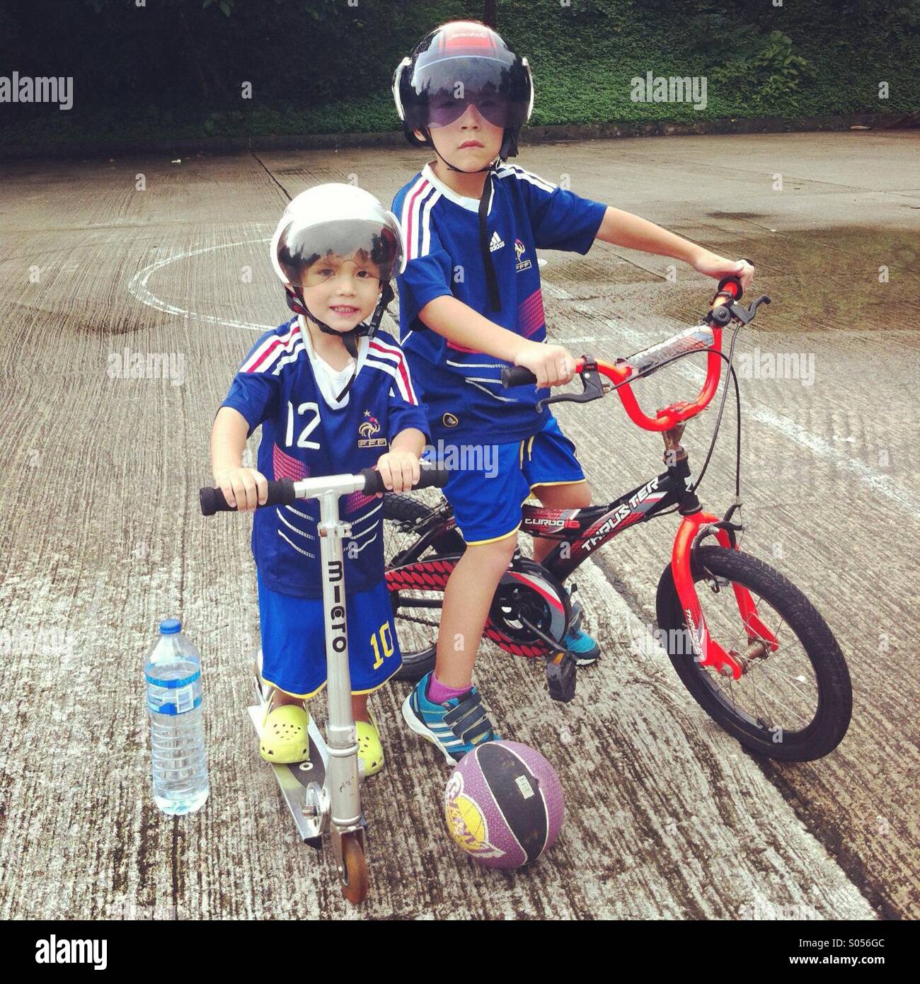 It's a photo of two brothers posing while riding a bicycle and a scooter. They wear the french football team jetsey Stock Photo
