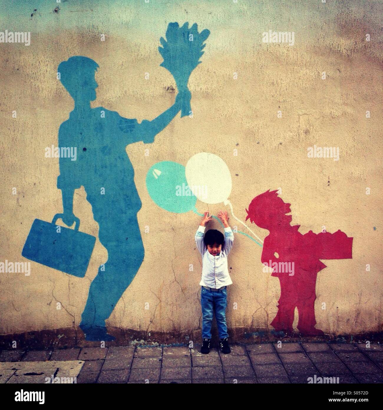 Little boy facing camera tries to reach for the balloon painted on the wall Stock Photo