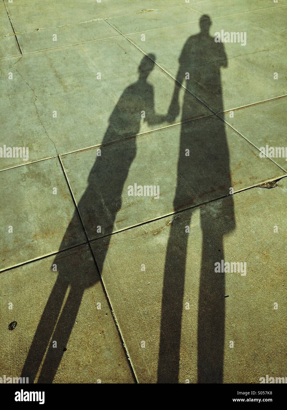 A father and son hold hands while standing and looking at their shadows Stock Photo