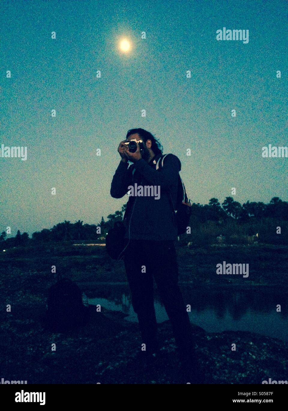 A man clicking photos at the seaside with the moon in the background Stock Photo