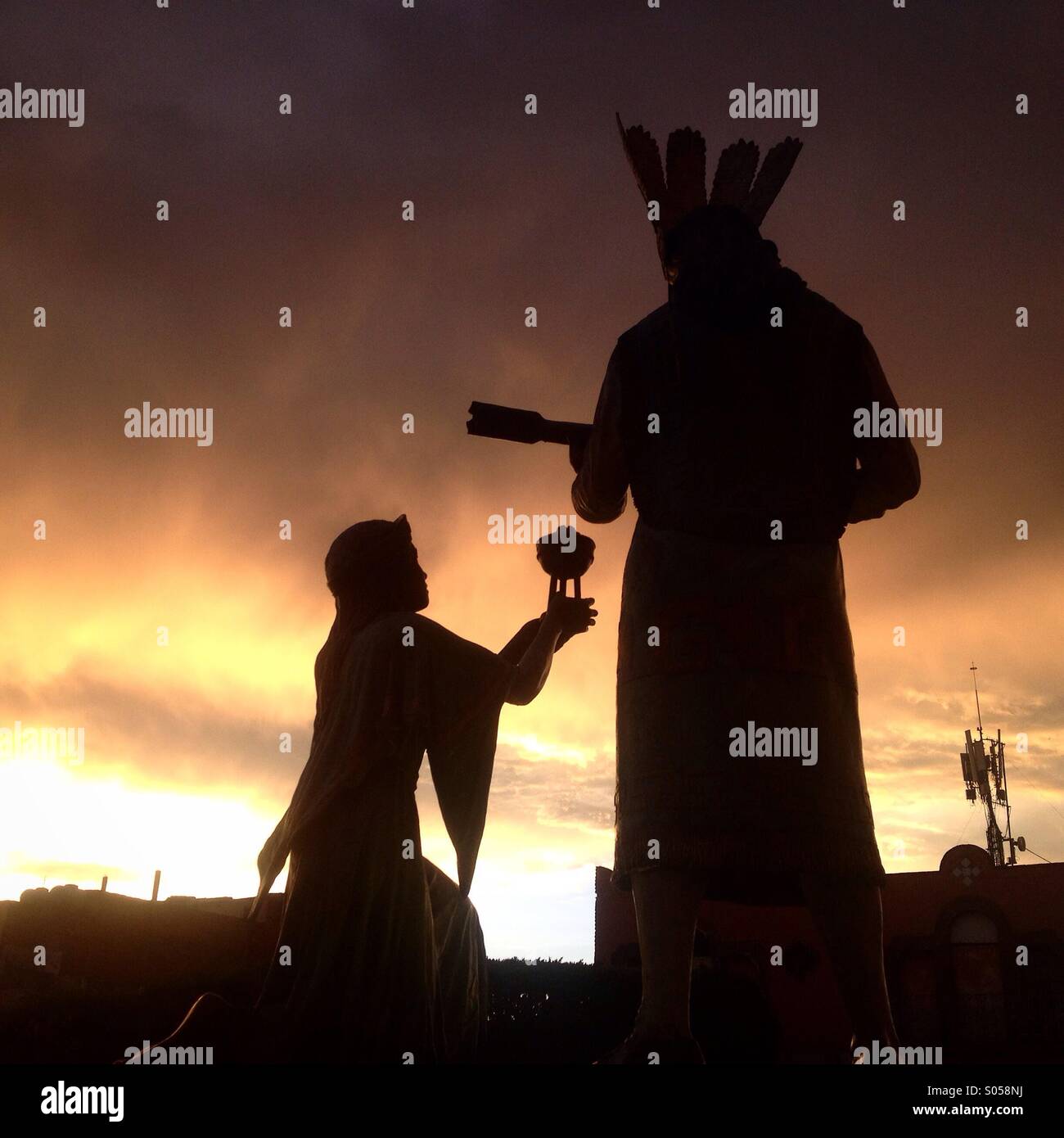 Silhouettes of sculptures of a Chichimeca indigenous woman offering copla incense and a danzante conchero dancer outside the Church of the Cross ( Iglesia de la cruz ) in Queretaro, Mexico. - Smartphone Captured Stock Image