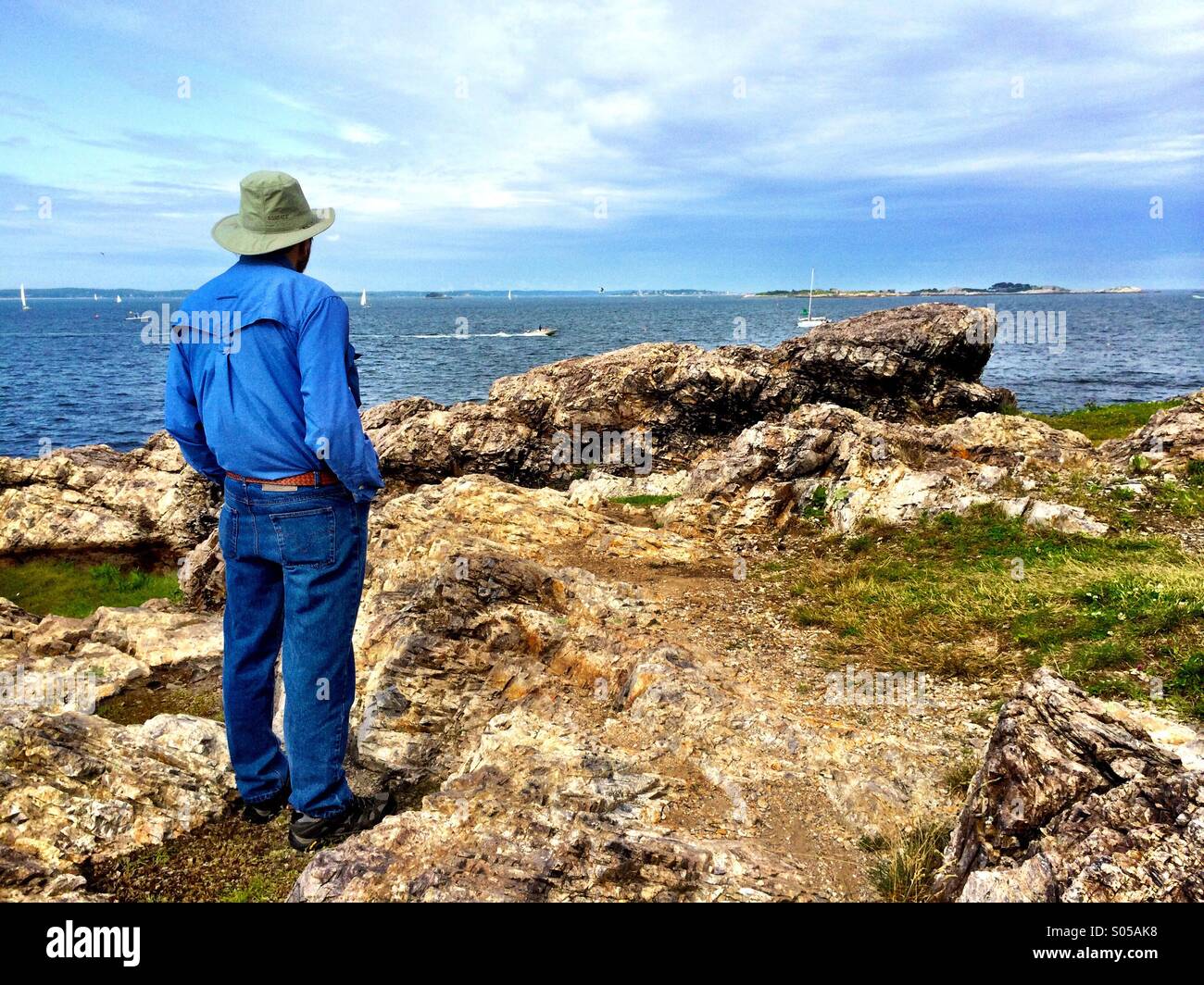 Man looks out toward the sea over rocks Stock Photo - Alamy