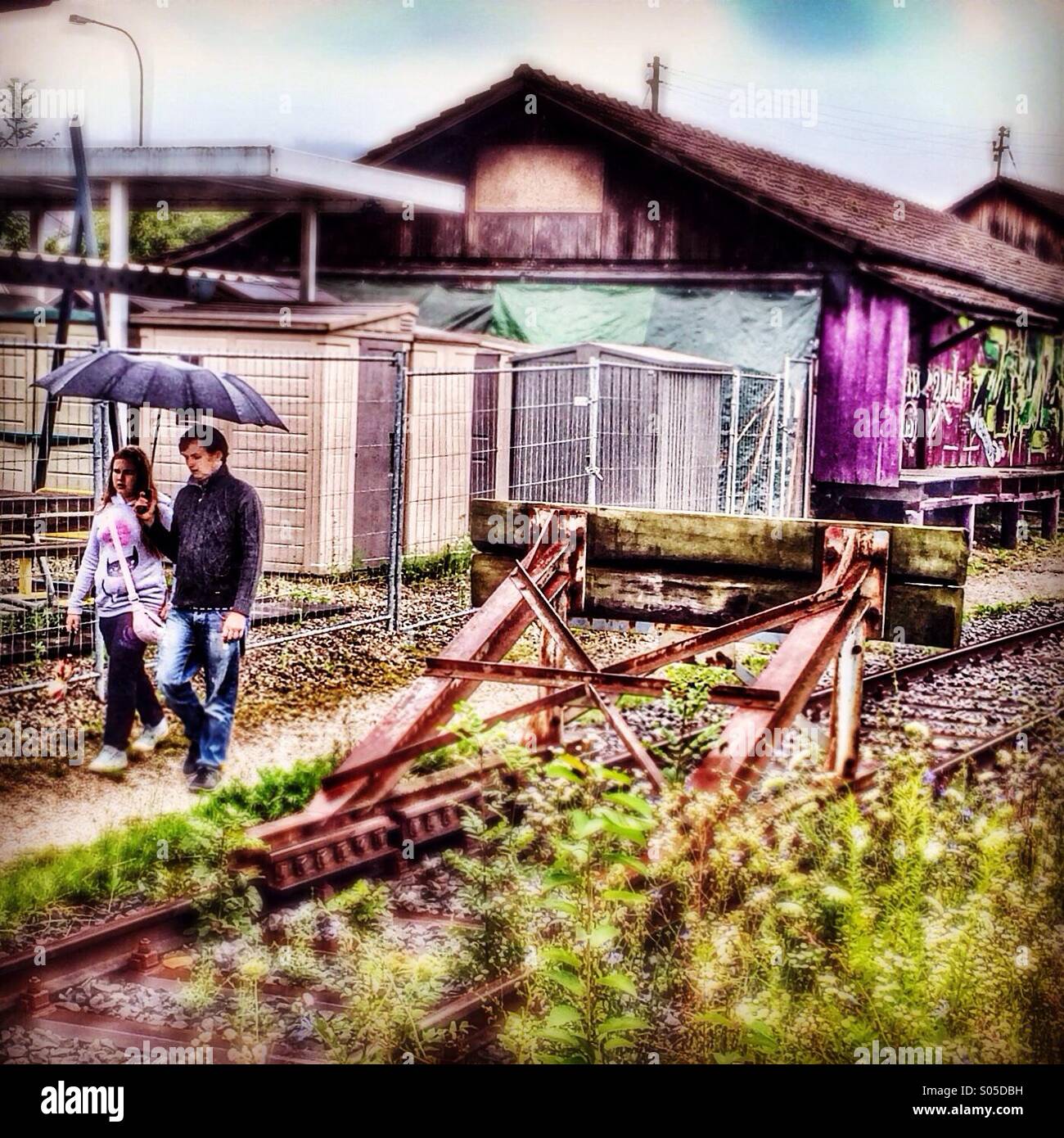 Couple with umbrella walking by railway tracks buffers Stock Photo - Alamy