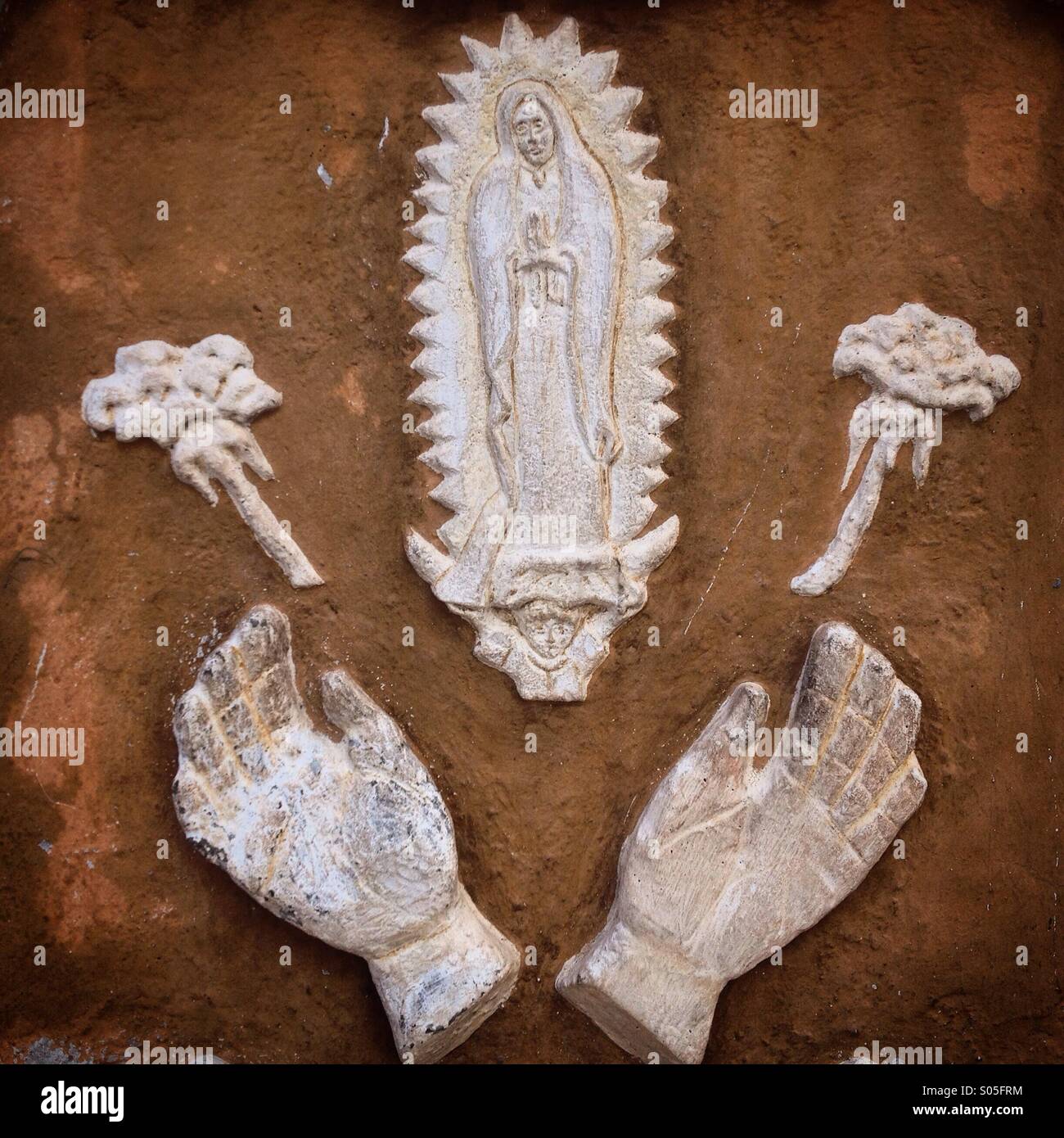 A white relief with the image of Our Lady of Guadalupe, two roses and two hands decorates the church of Peña de Bernal, Queretaro state, Mexico - Smartphone Captured Stock Image