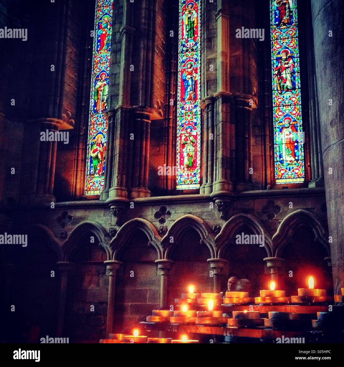 Candles burning in a church in front of stain glass windows. - Smartphone Captured Stock Image