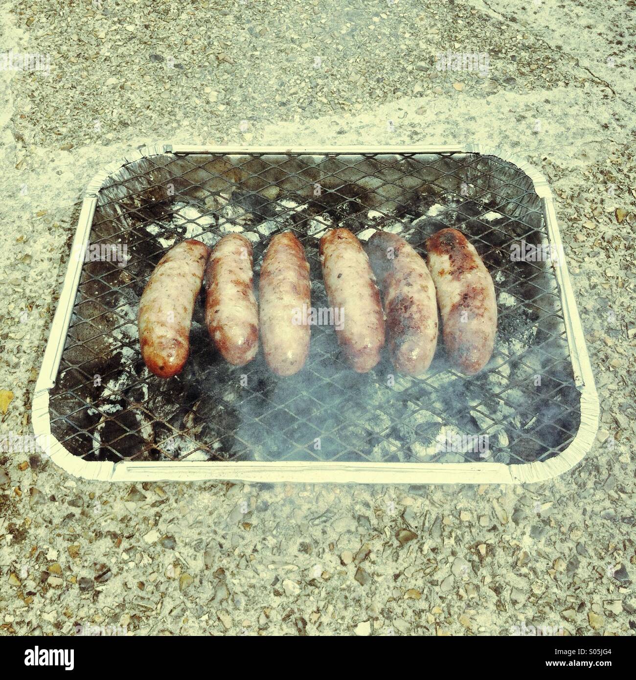 Grilling sausages over an open flame at an outdoor gathering during summer afternoon in the backyard - Smartphone Captured Stock Image