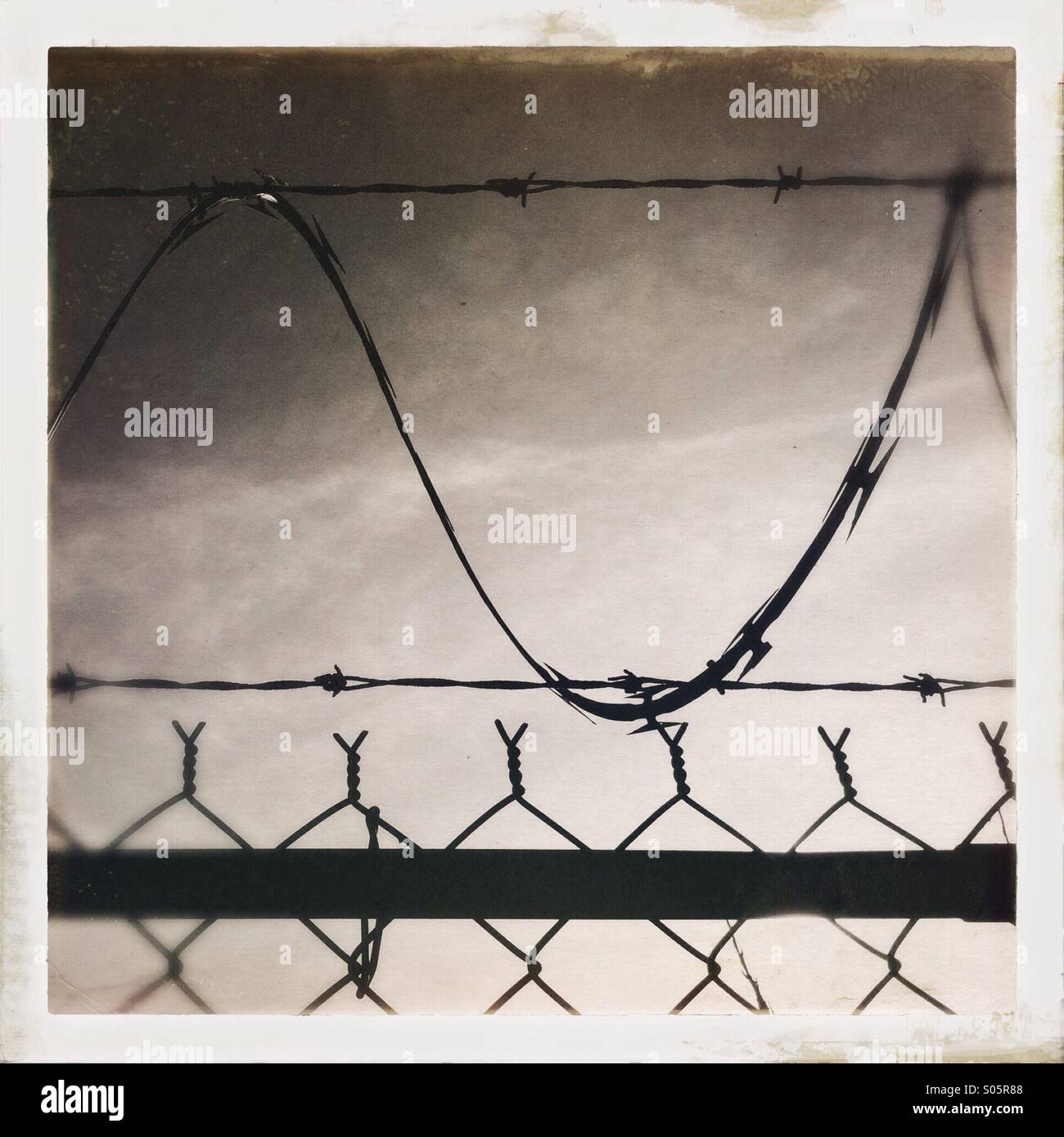 Silhouette of razor wire and chain link wire fence. - Smartphone Captured Stock Image