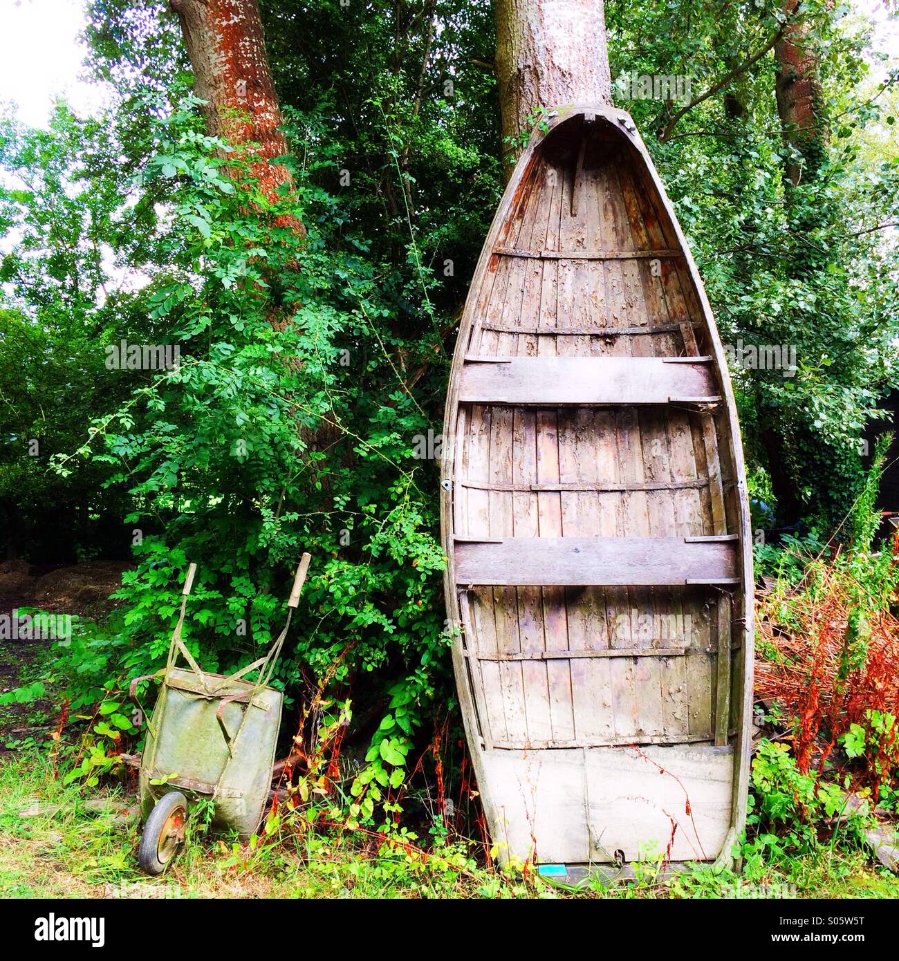 Old wooden boat and wheelbarrow in a garden Stock Photo