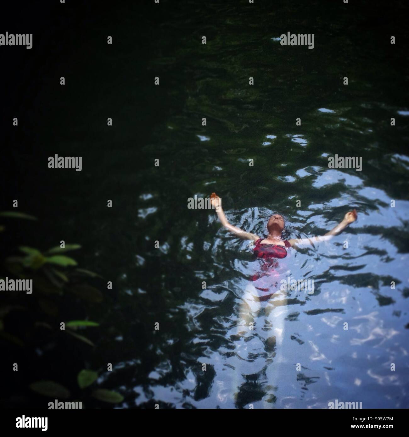 A woman swims in Cenote Xcanche a natural cave pool, called Cenote en maya, near Ek Balam Mayan city in Tizimin, Yucatan, Mexico - Smartphone Captured Stock Image