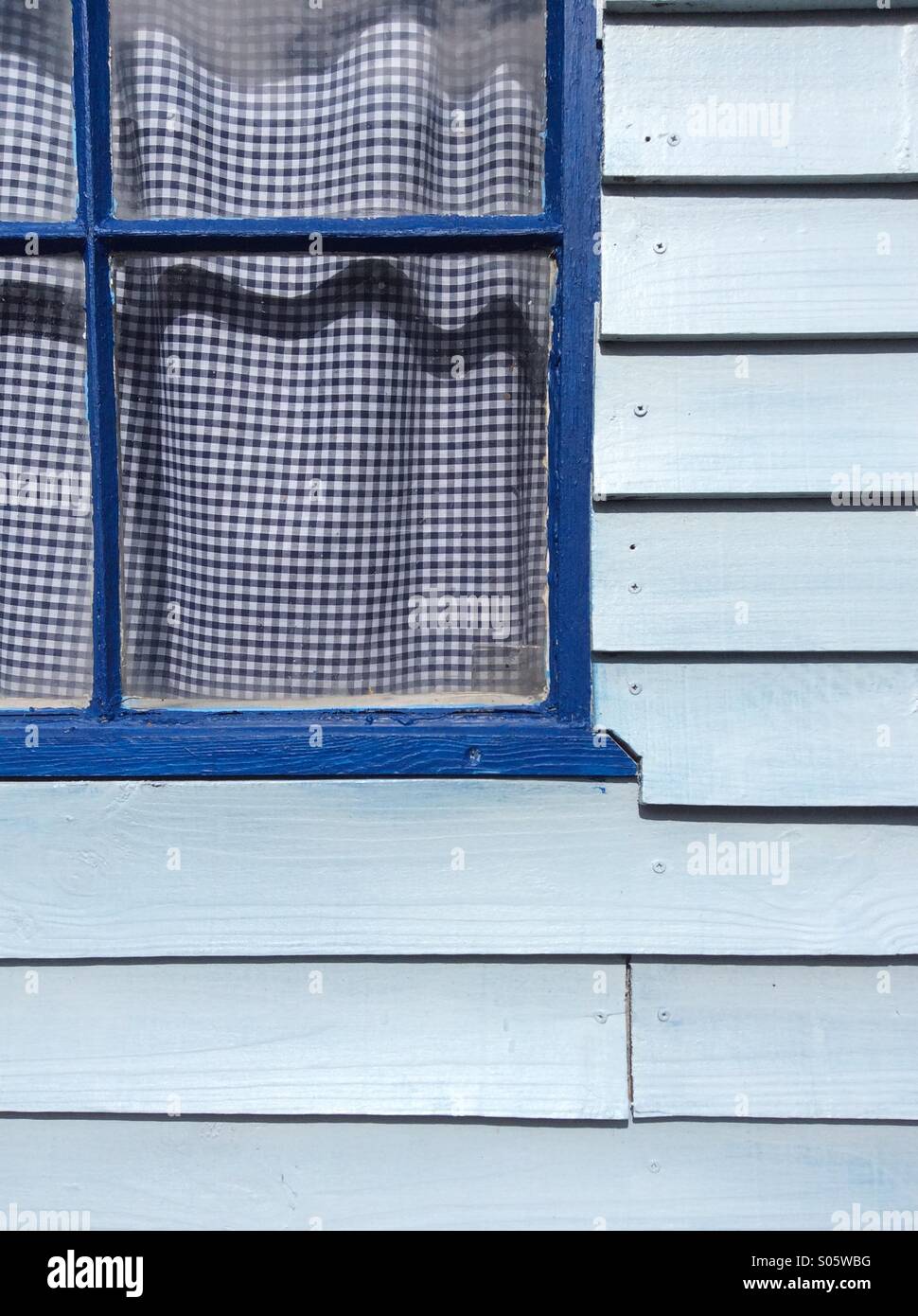 Blue clapboard shed with blue window frame and blue gingham curtains. Stock Photo