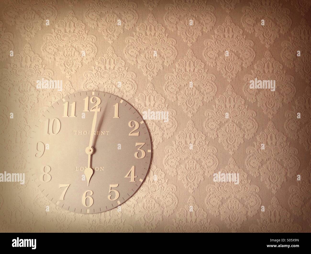 A clock on a wall with old fashioned wallpaper Stock Photo