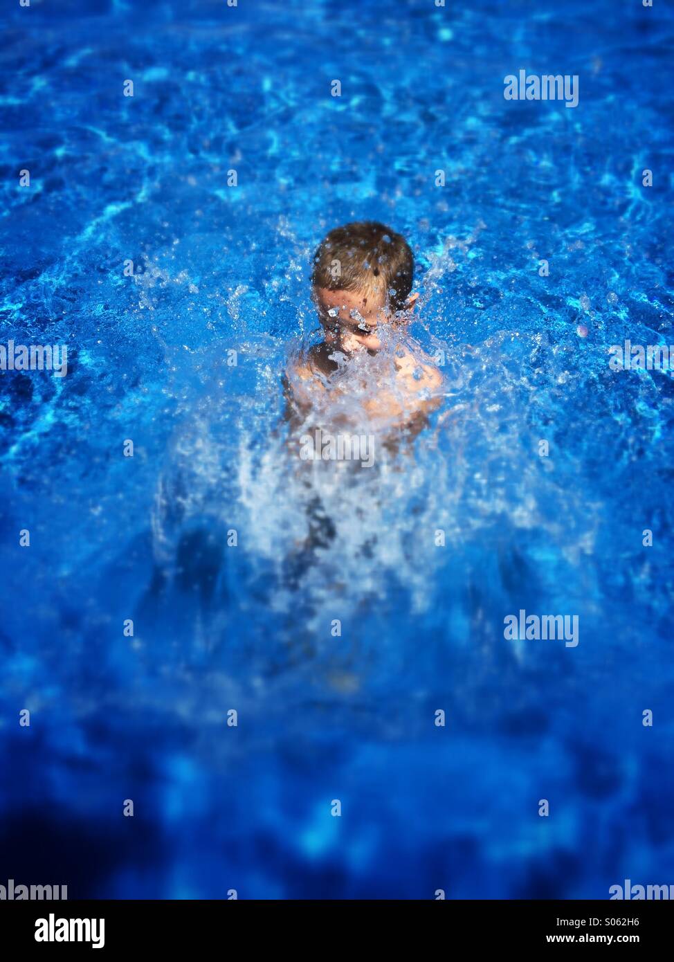 A young boy splashes in a deep blue pool Stock Photo
