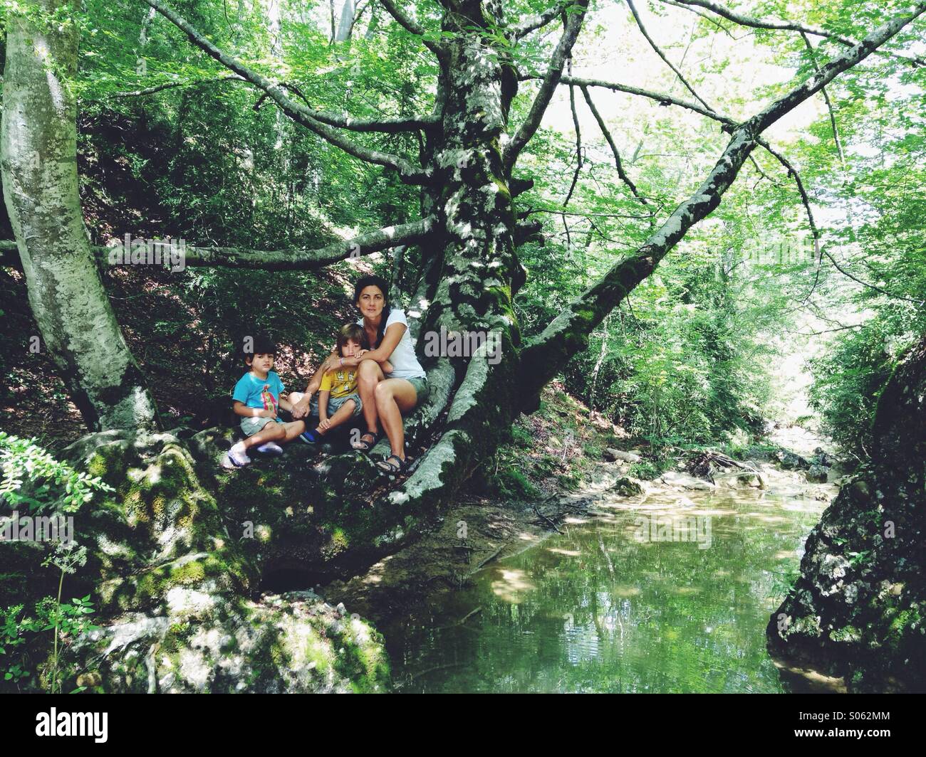 Young woman and two children on a tree next two a river Stock Photo